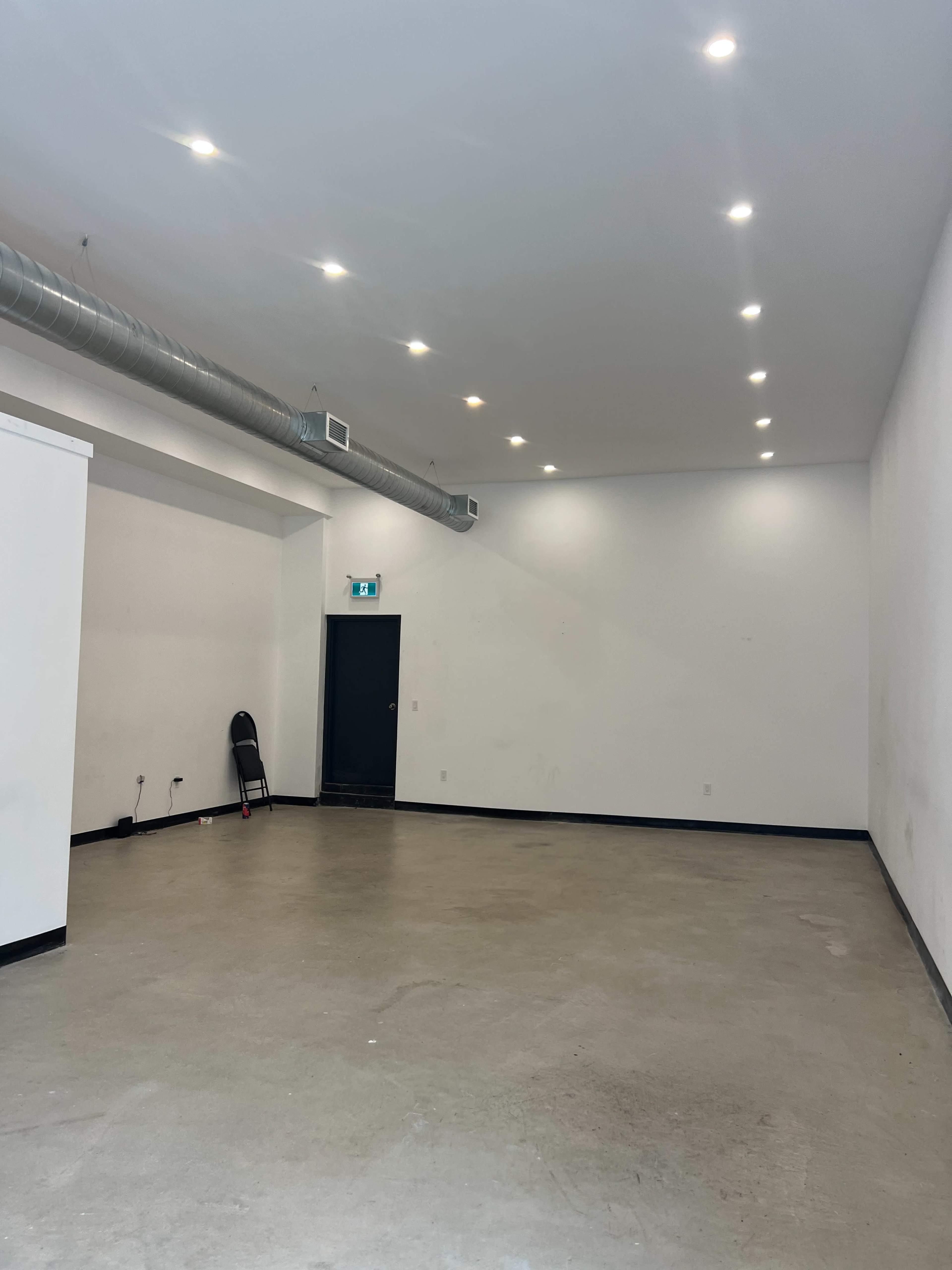 A large, empty room with smooth concrete floors, white walls, and a black door at one end.