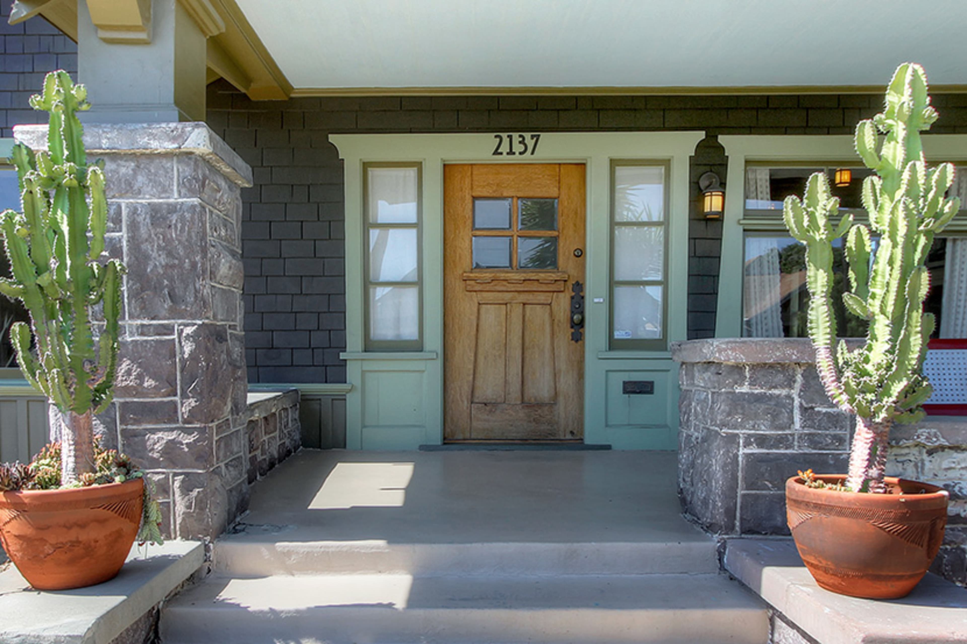 The entrance features a wooden front door with a window panel, flanked by two potted cacti on the porch.