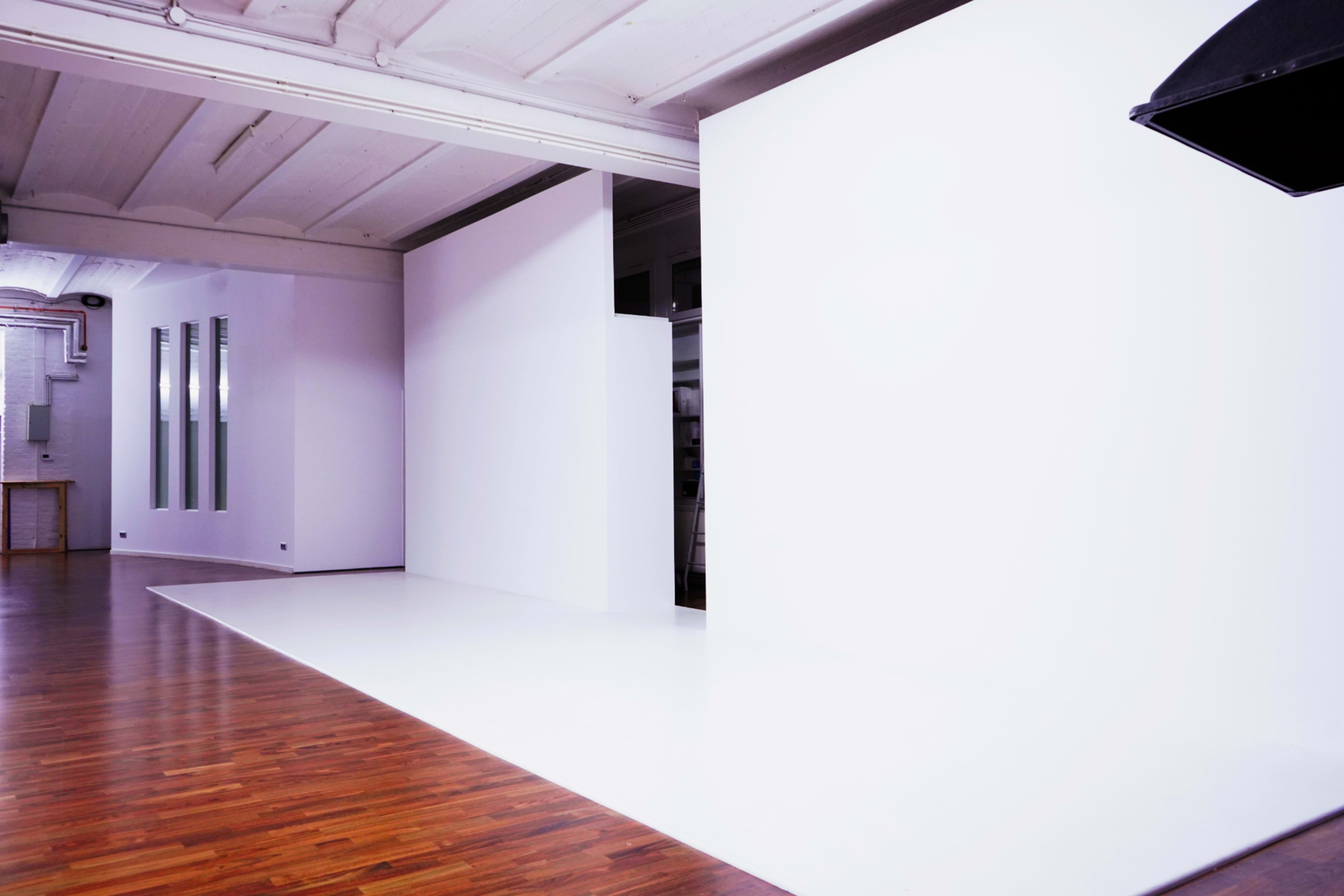 The image shows a spacious, empty studio with white walls and polished wooden flooring.