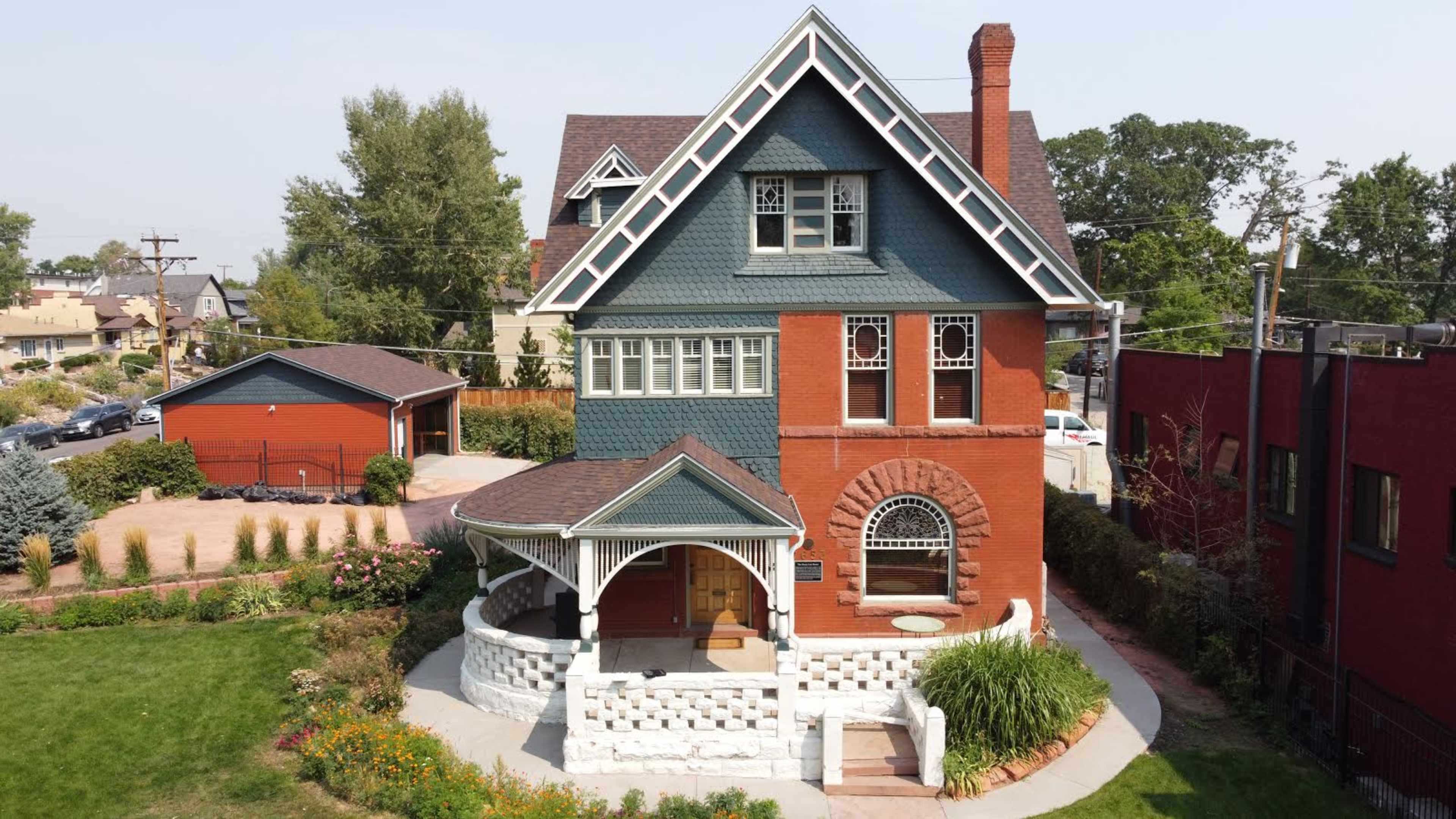 A large, two-story house features a mix of brick and shingle siding with a wraparound porch and landscaped yard.
