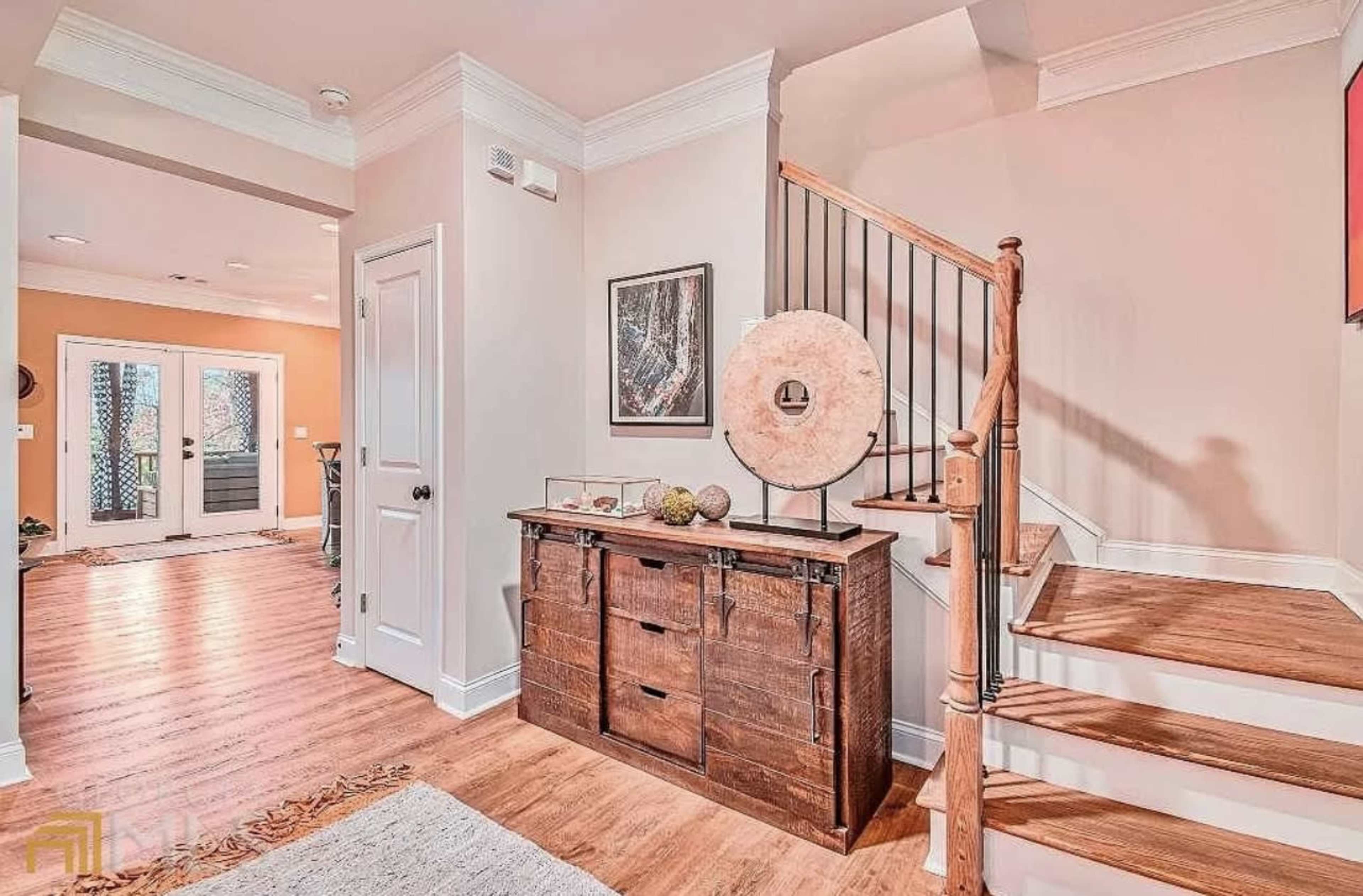 The image depicts an interior hallway featuring a wooden cabinet, a staircase leading to the upper level, and an entrance to a room with a warm, inviting color scheme.