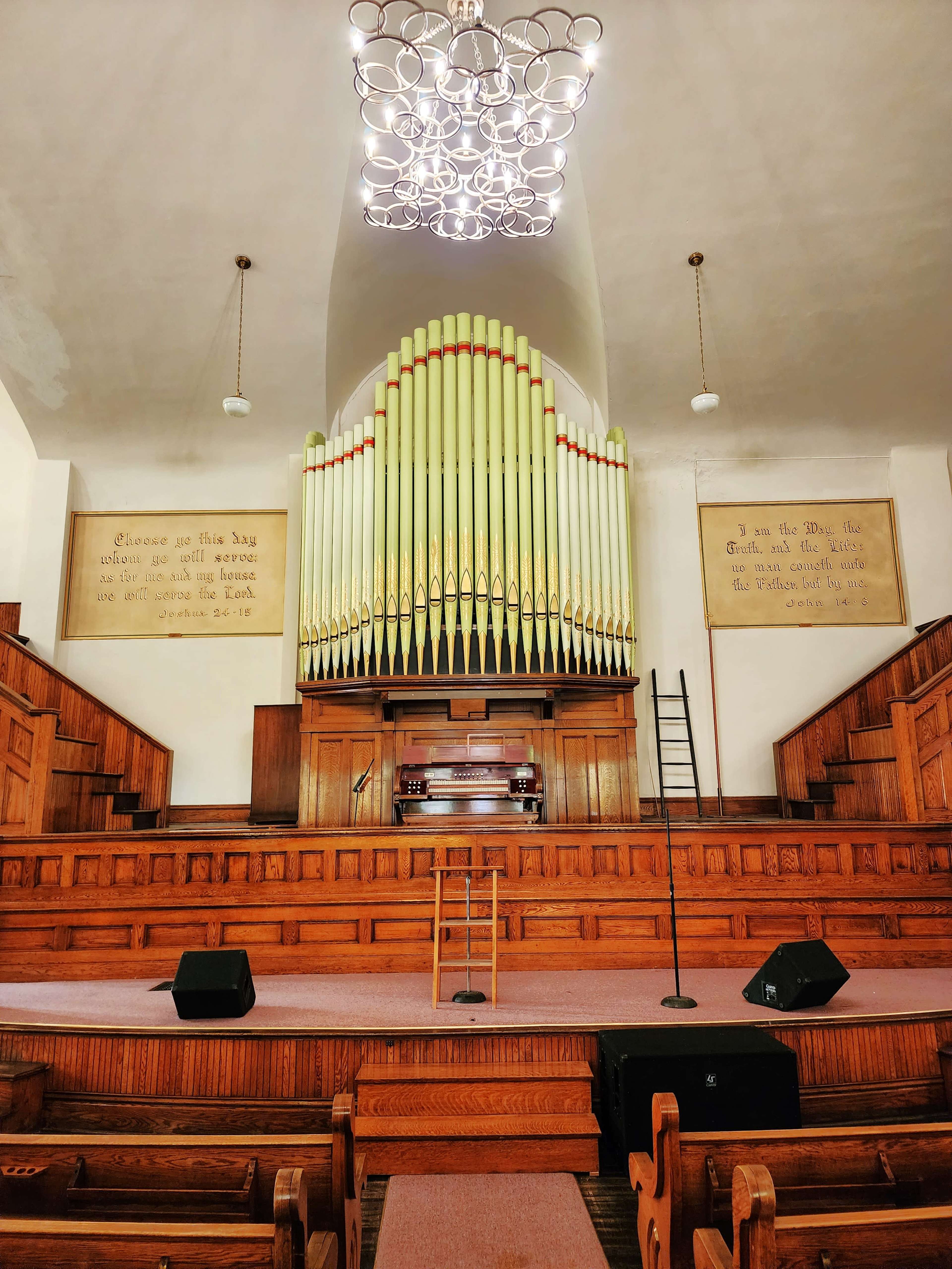 The interior of a church featuring a large pipe organ above a wooden stage with empty seating and decorations on the walls.