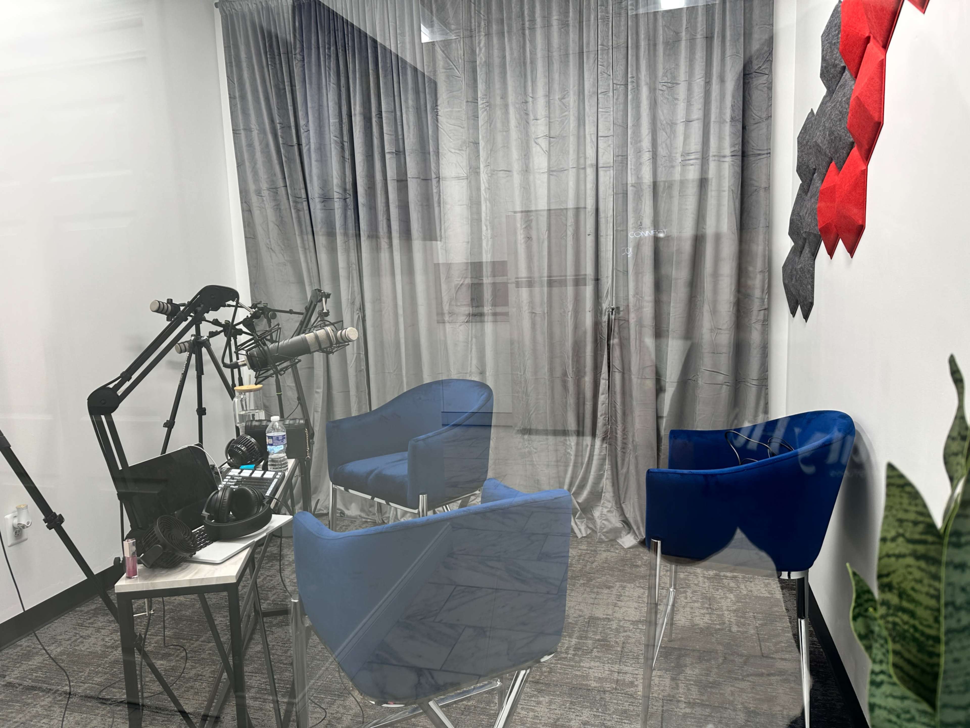 A recording studio with blue chairs, microphones on stands, and a backdrop of gray curtains.