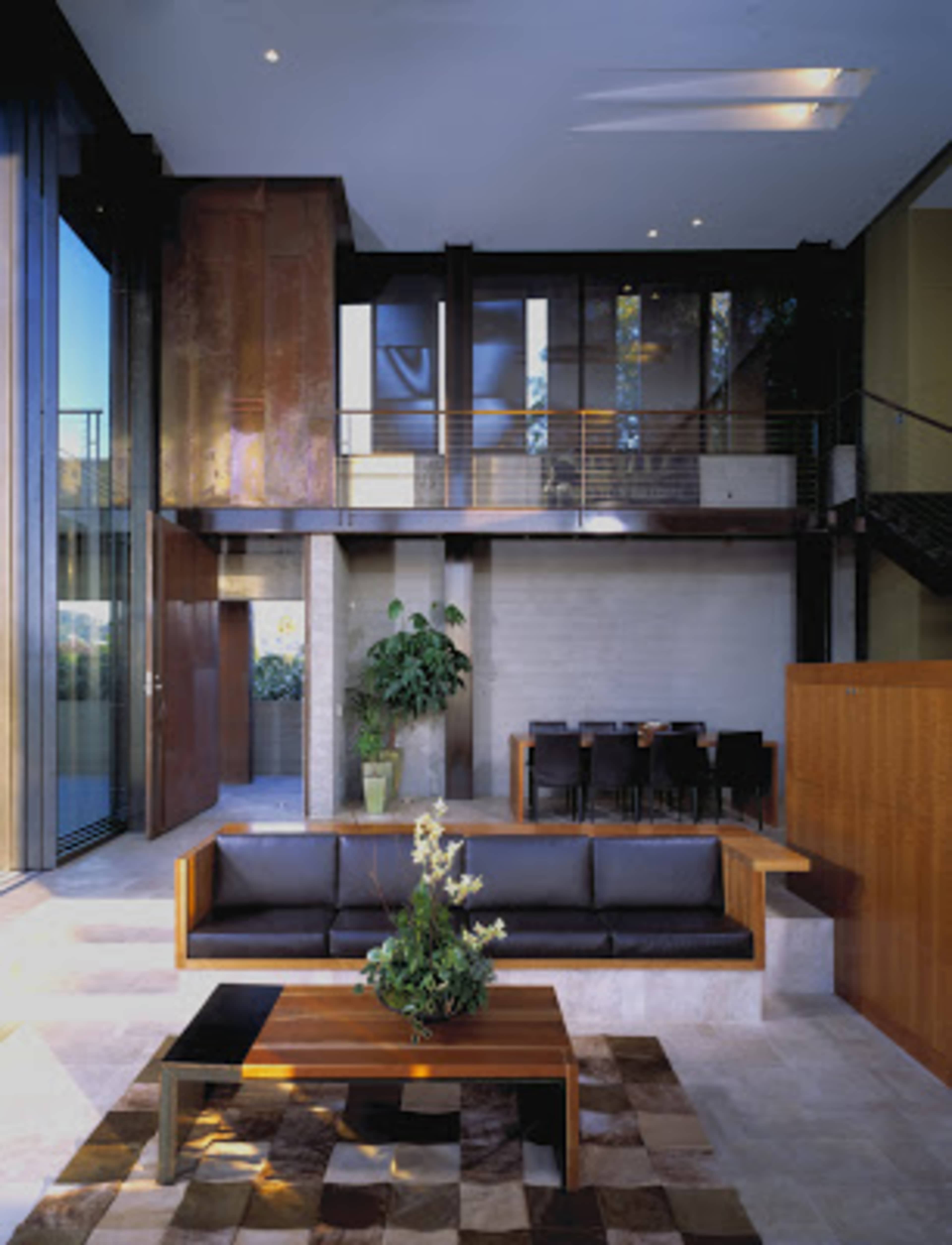 A modern living room with a black sofa, a wooden coffee table, and large windows that provide a view of the outdoors.