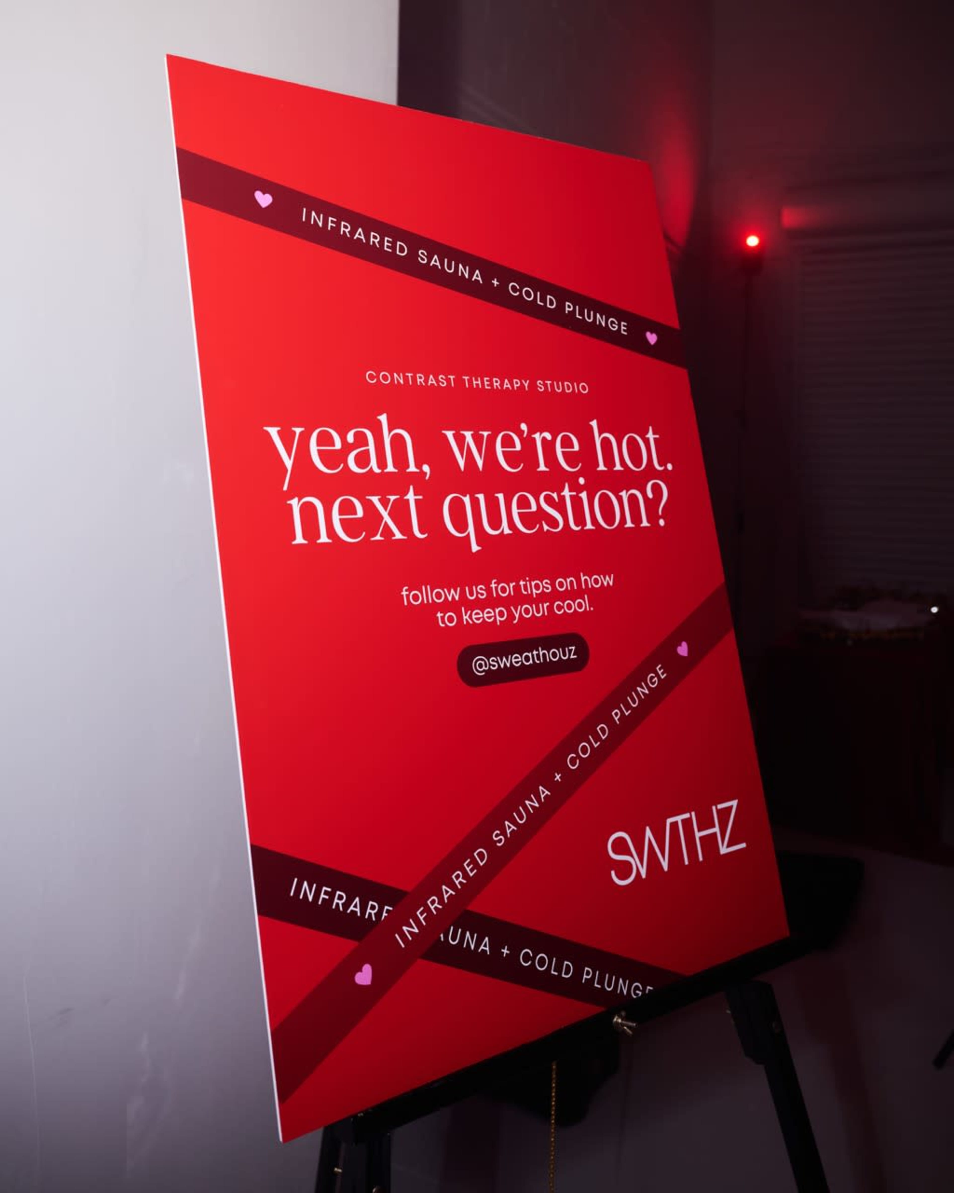 The image shows a promotional sign for a contrast therapy studio featuring a red background and text that highlights infrared saunas and cold plunges.