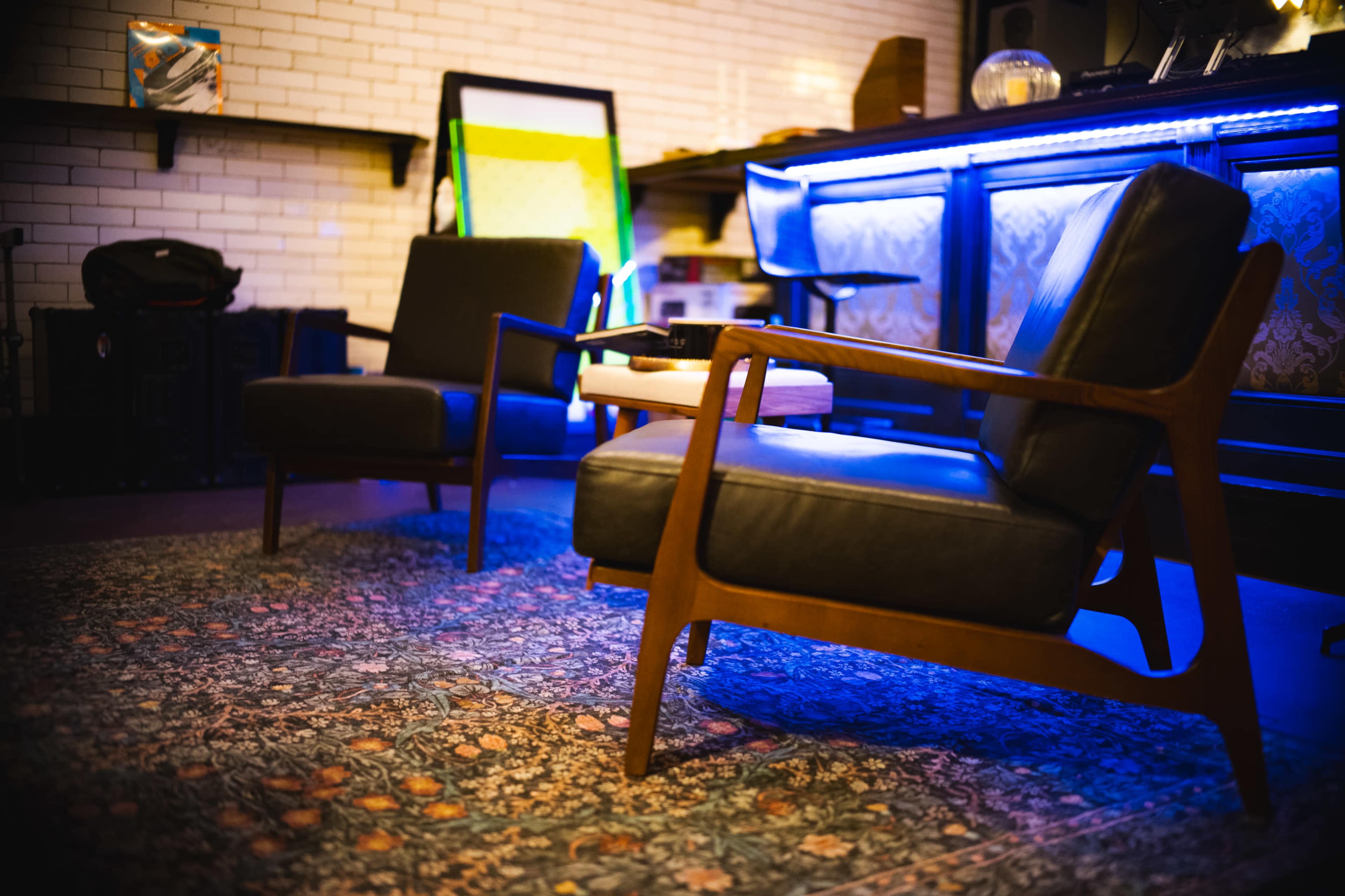 The image shows two mid-century modern chairs positioned in front of a bar area, with a decorative rug and ambient lighting.