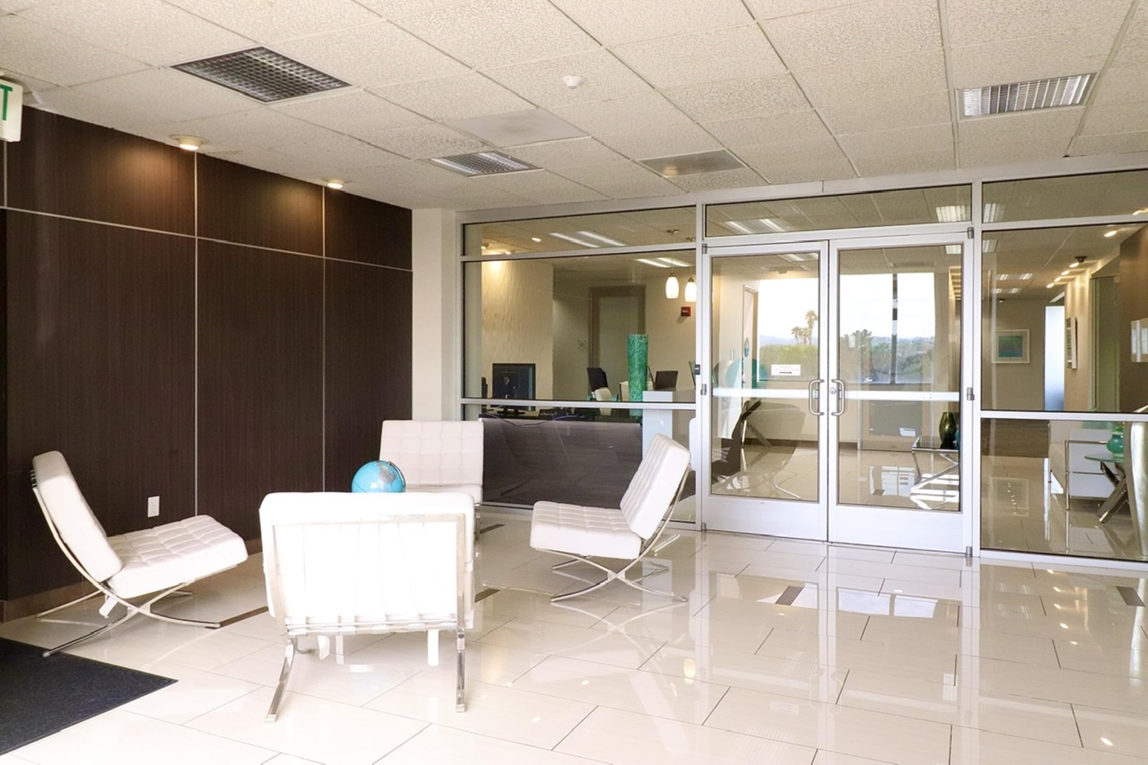 A modern reception area with white furniture, large glass doors, and a tiled floor.