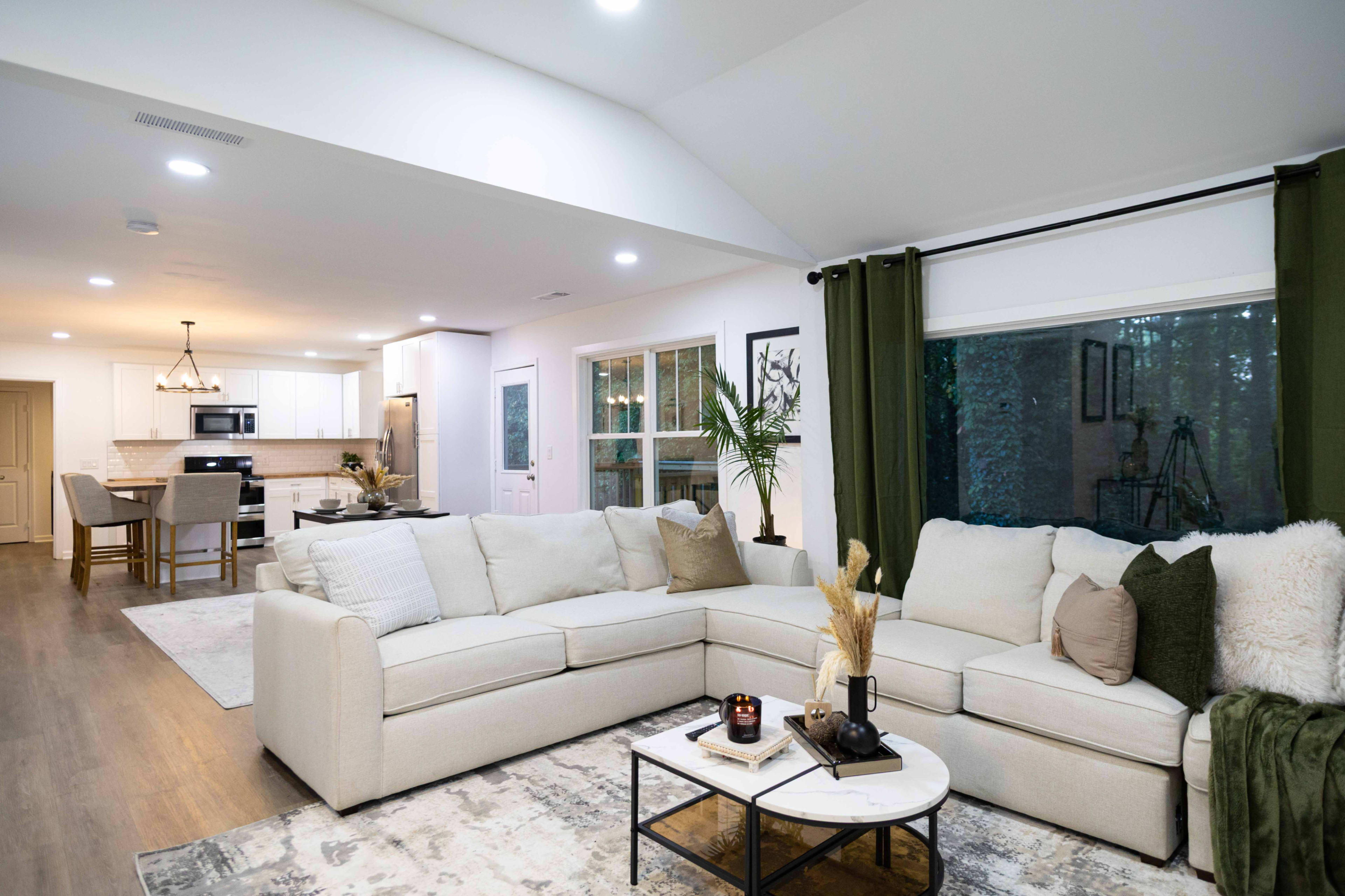 A spacious living area features a large sectional sofa, a coffee table, and an open kitchen with modern appliances visible in the background.