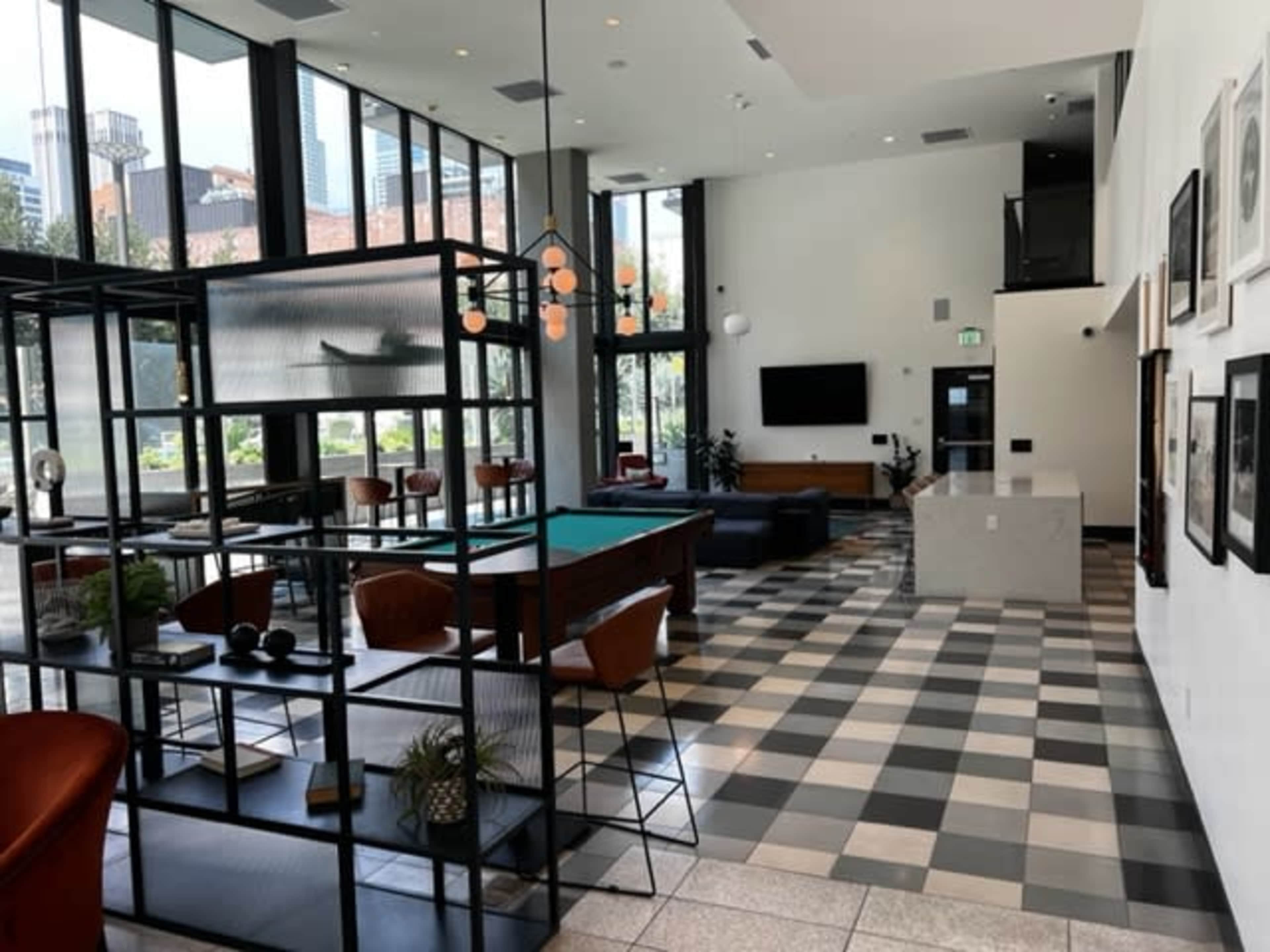 The image shows a modern lounge area featuring large windows, a pool table, seating arrangements, and a small reception area.