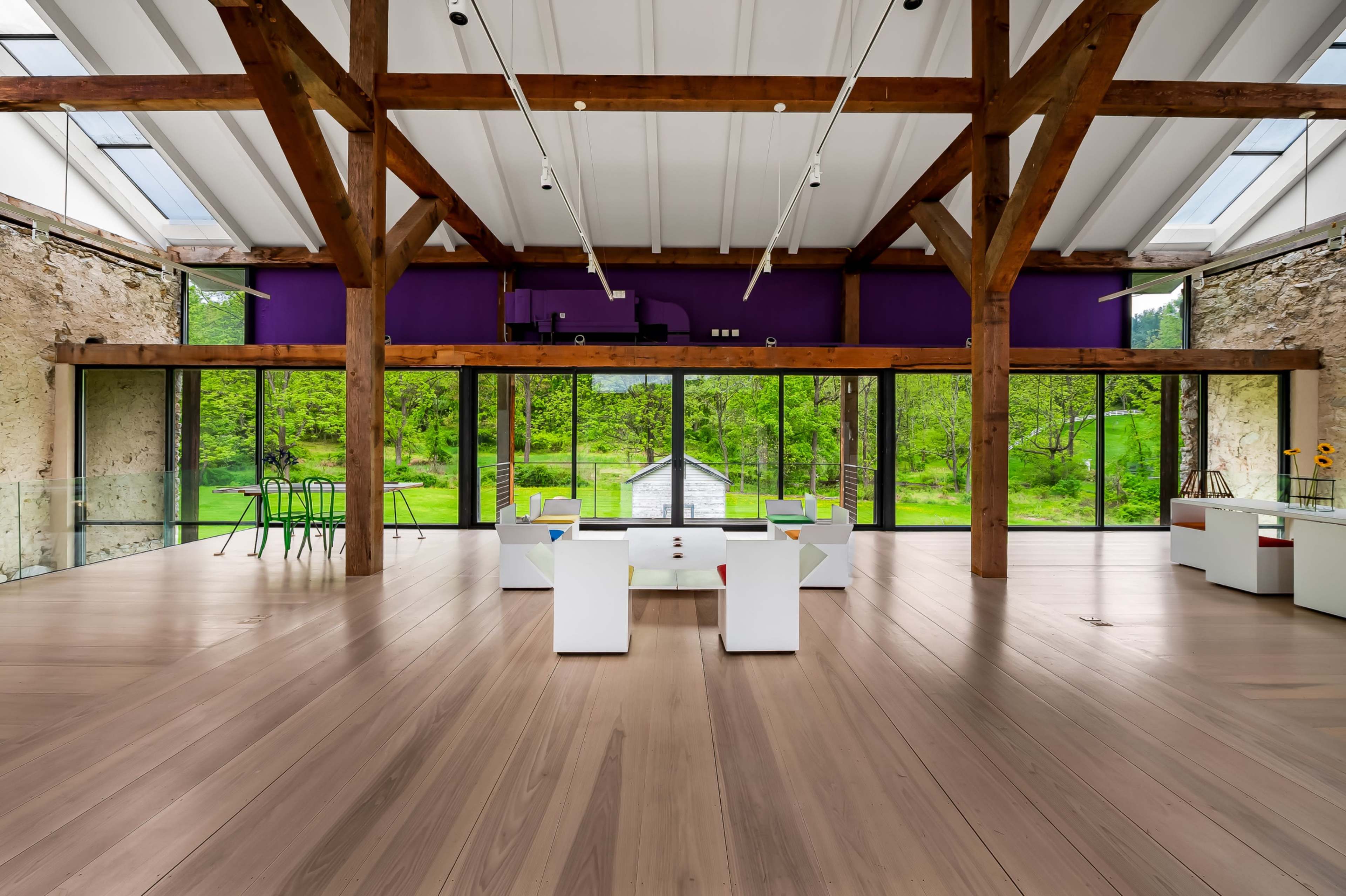The image features an open, modern interior space with high wooden beams, large glass windows, and a view of greenery outside.