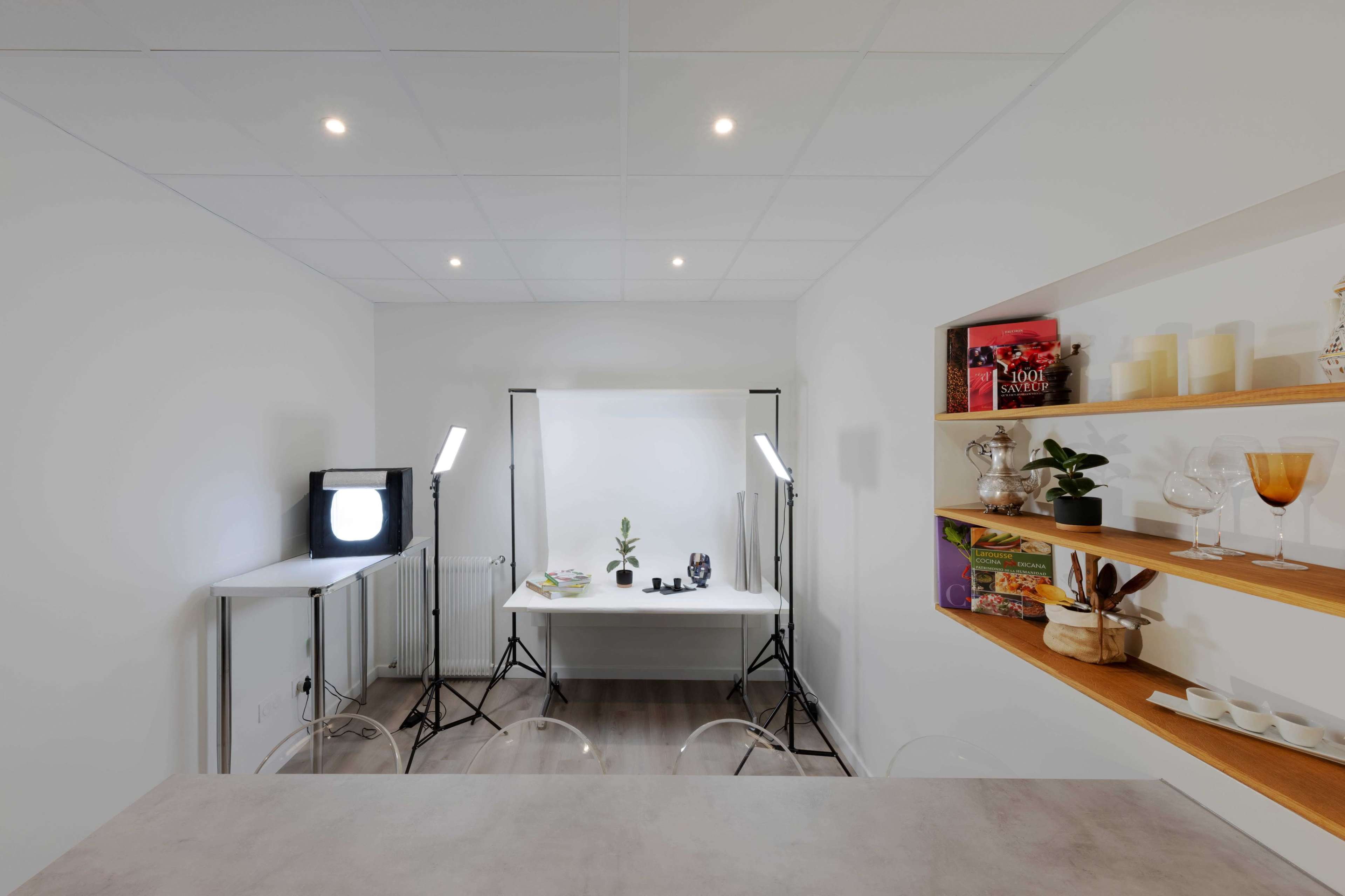 A well-lit studio space with a table, photography equipment, and styled shelves displaying decorative items.