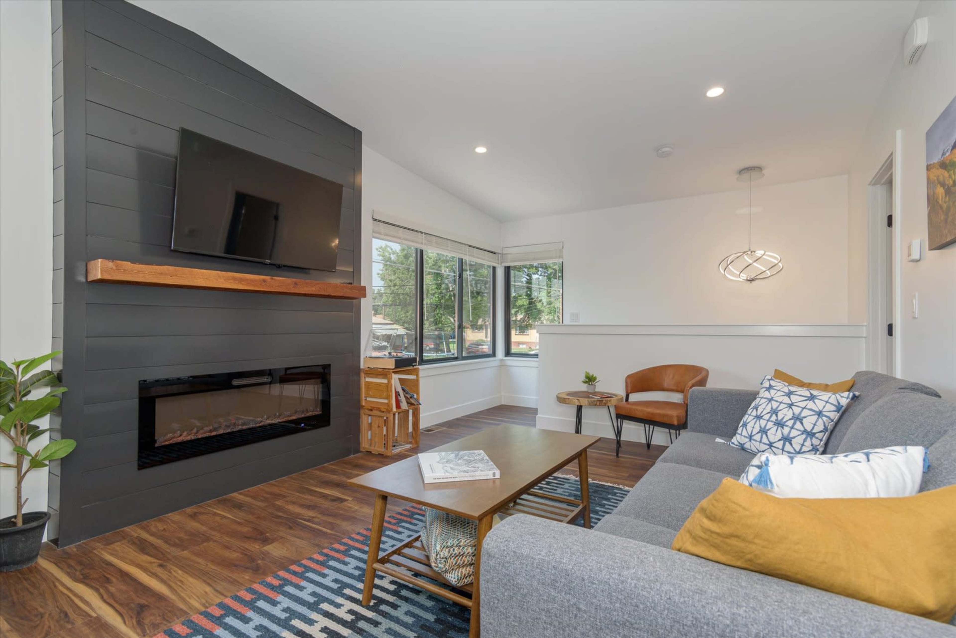 A modern living room featuring a gray sofa, a wooden coffee table, a wall-mounted television, and large windows that let in natural light.