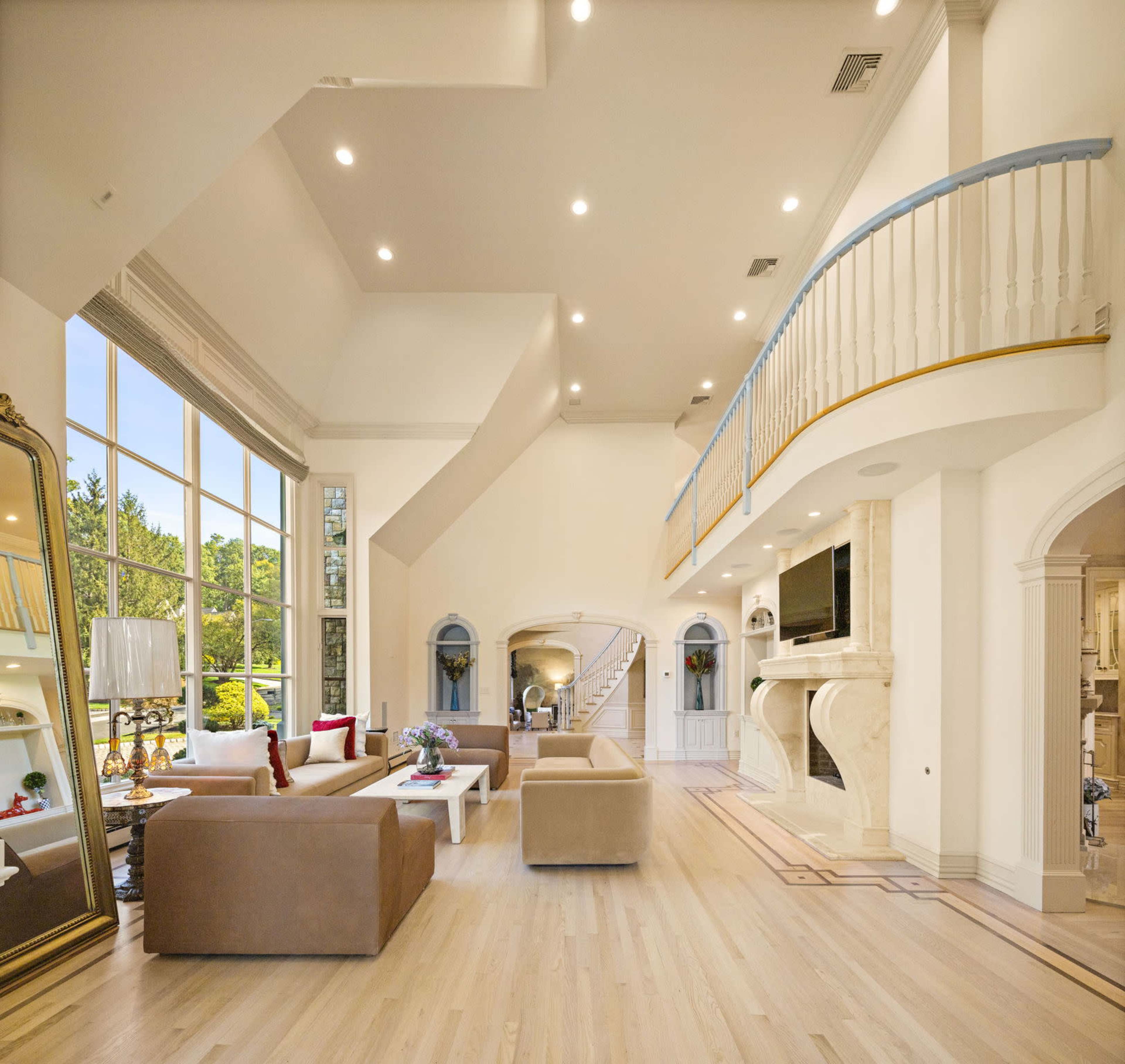 The interior of a spacious and brightly lit living room features large windows, a balcony, and modern furnishings.
