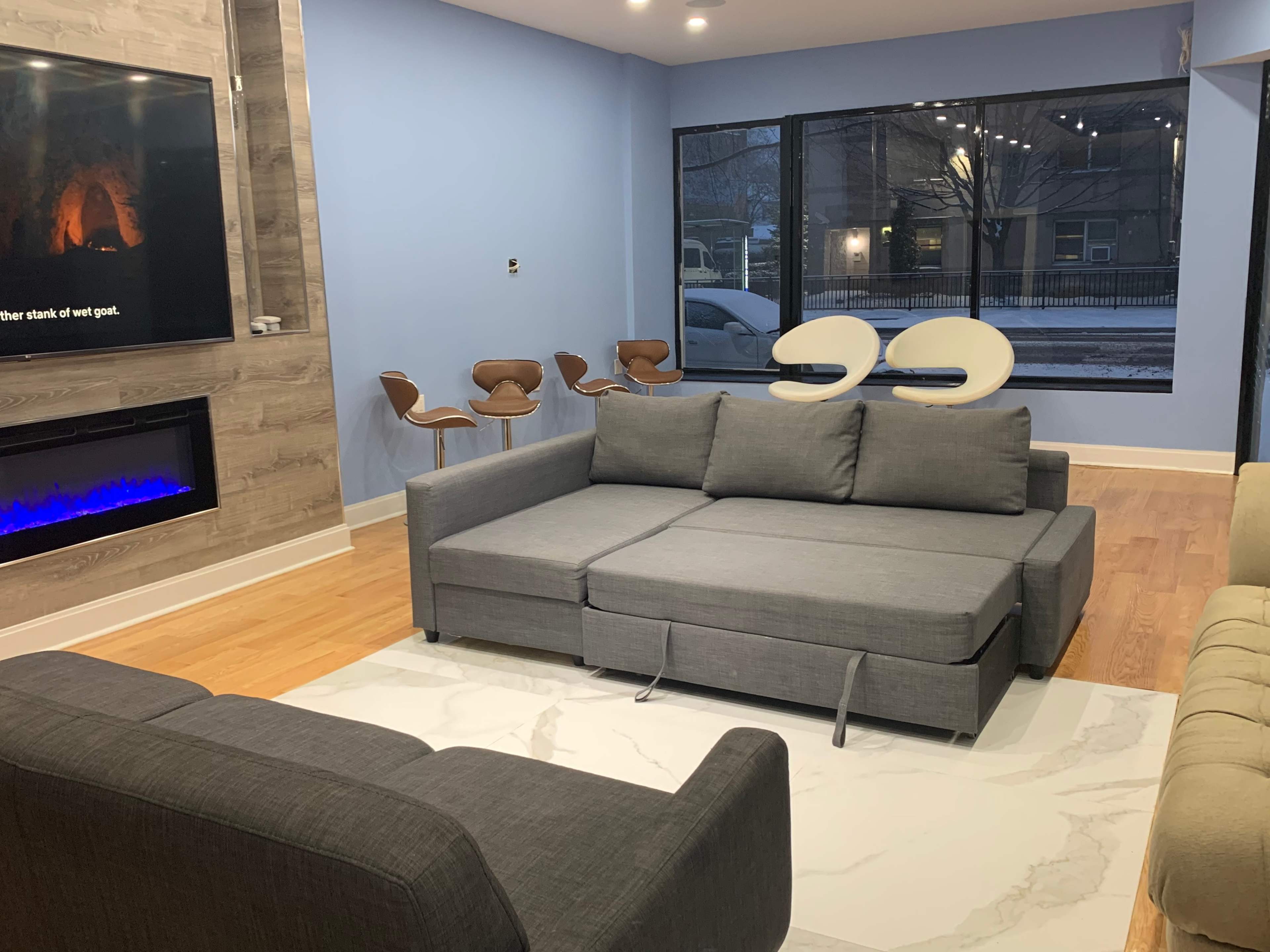 A modern living room with a gray sectional sofa, a white rug, and a set of stylish chairs near a large window.