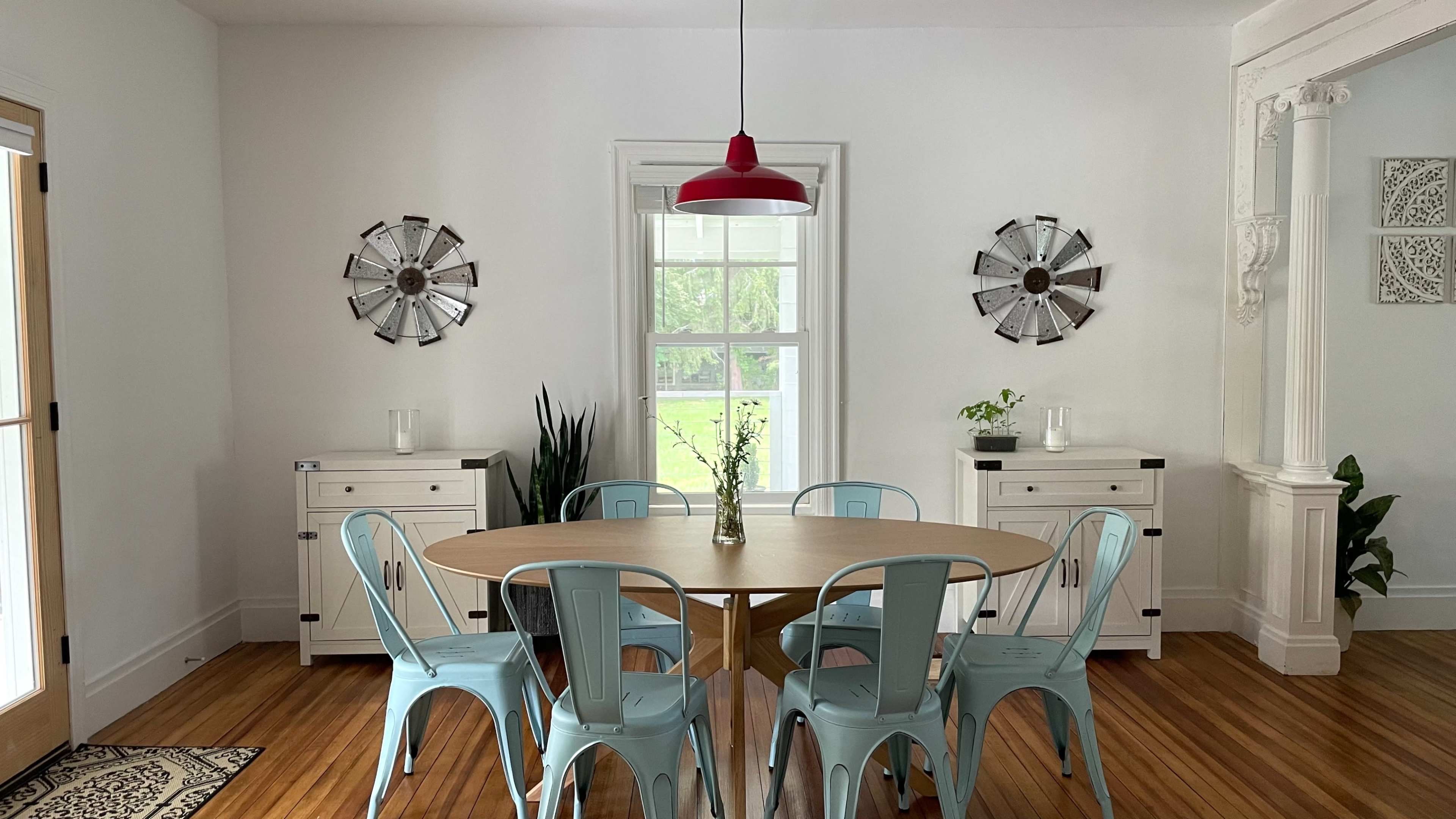 A dining area with a round wooden table surrounded by blue metal chairs, set against a backdrop of white walls and decorative wall features.