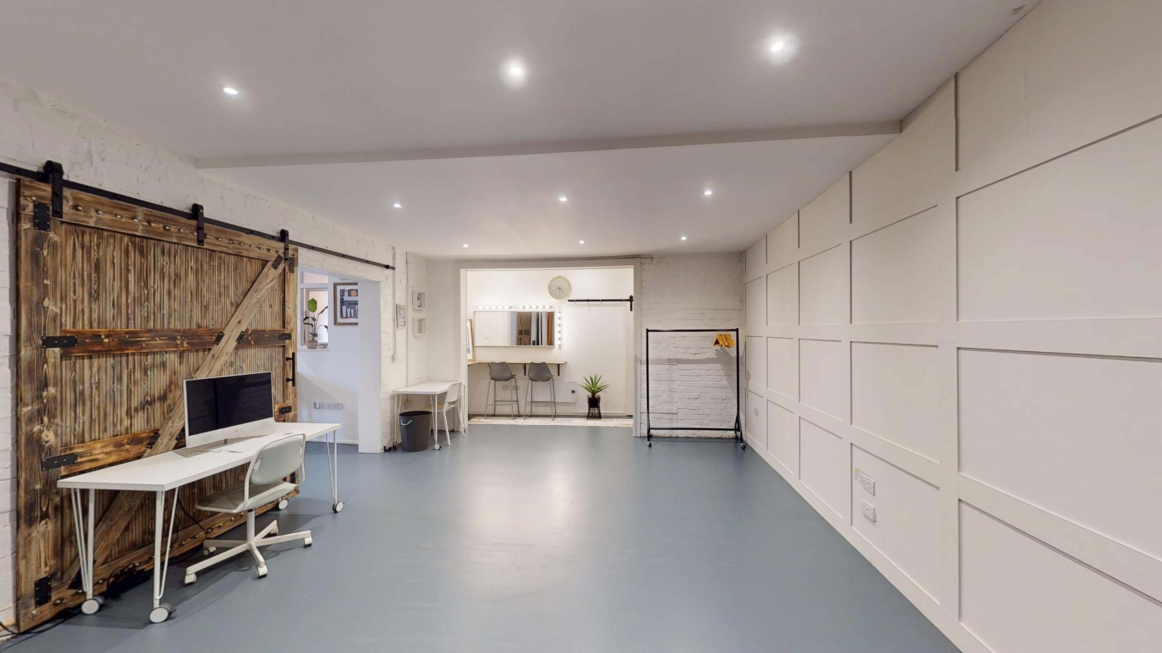 The image shows a spacious, well-lit room with a wooden sliding door, a desk with a computer, and a mirror setup against a white wall.