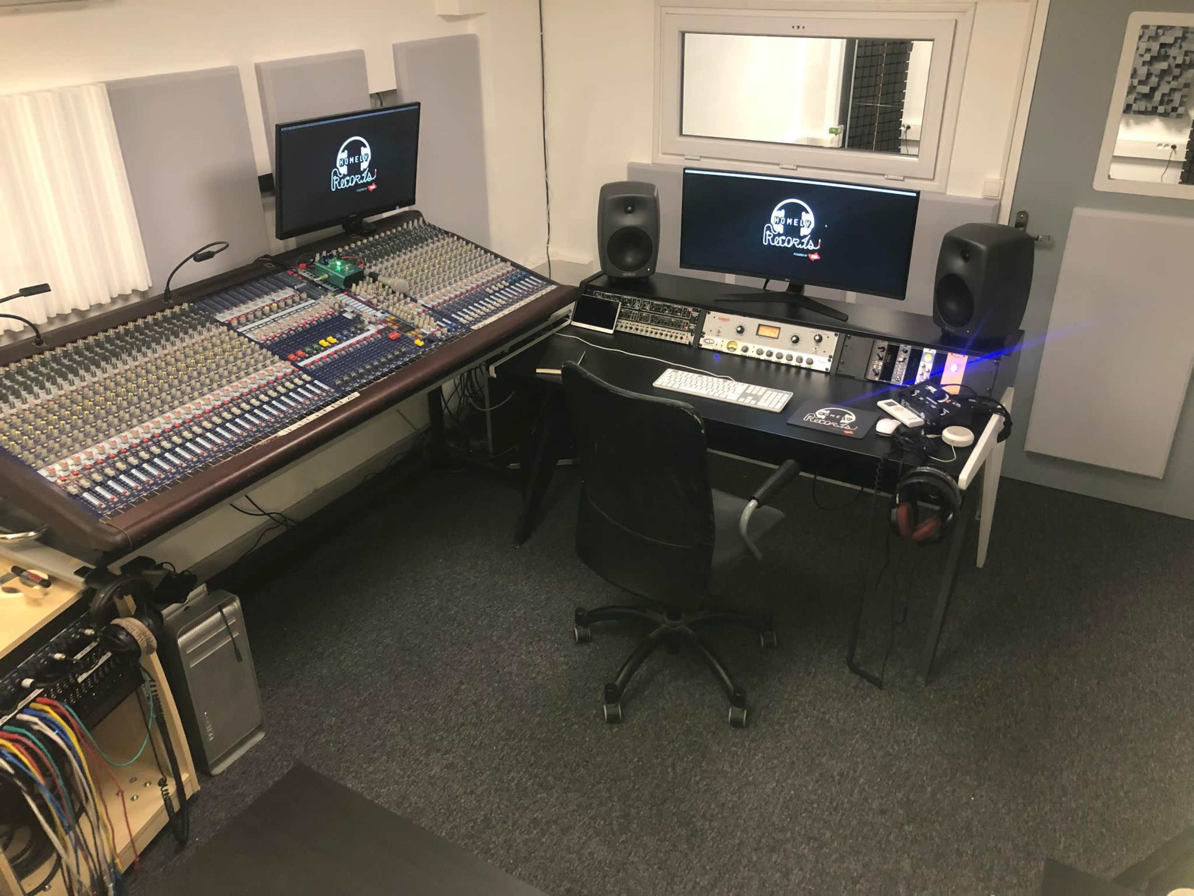 A modern audio recording studio featuring a large mixer, computer monitors, and various audio equipment.