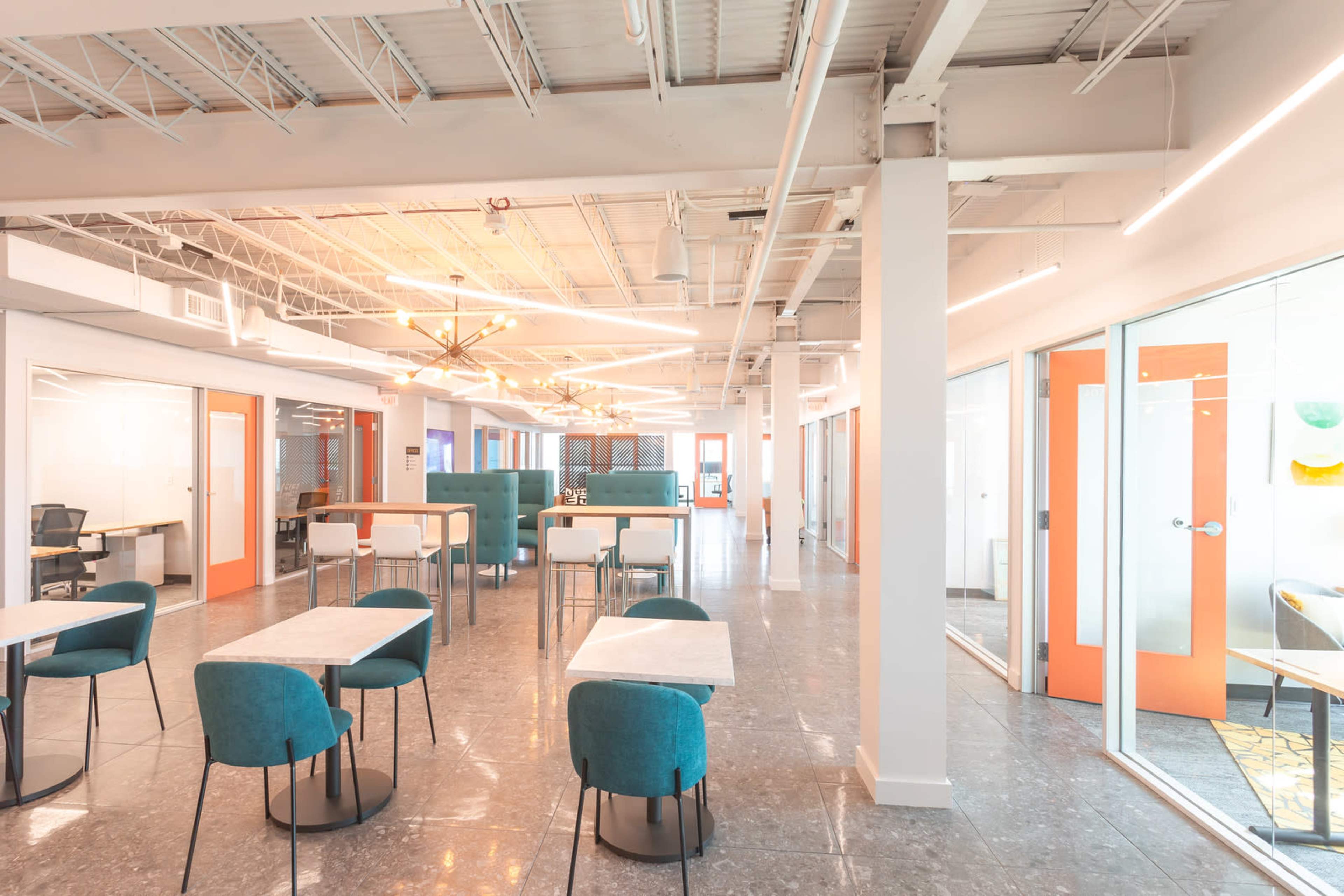 The image shows a modern office space with tables, teal chairs, and glass-walled meeting rooms featuring orange doors.