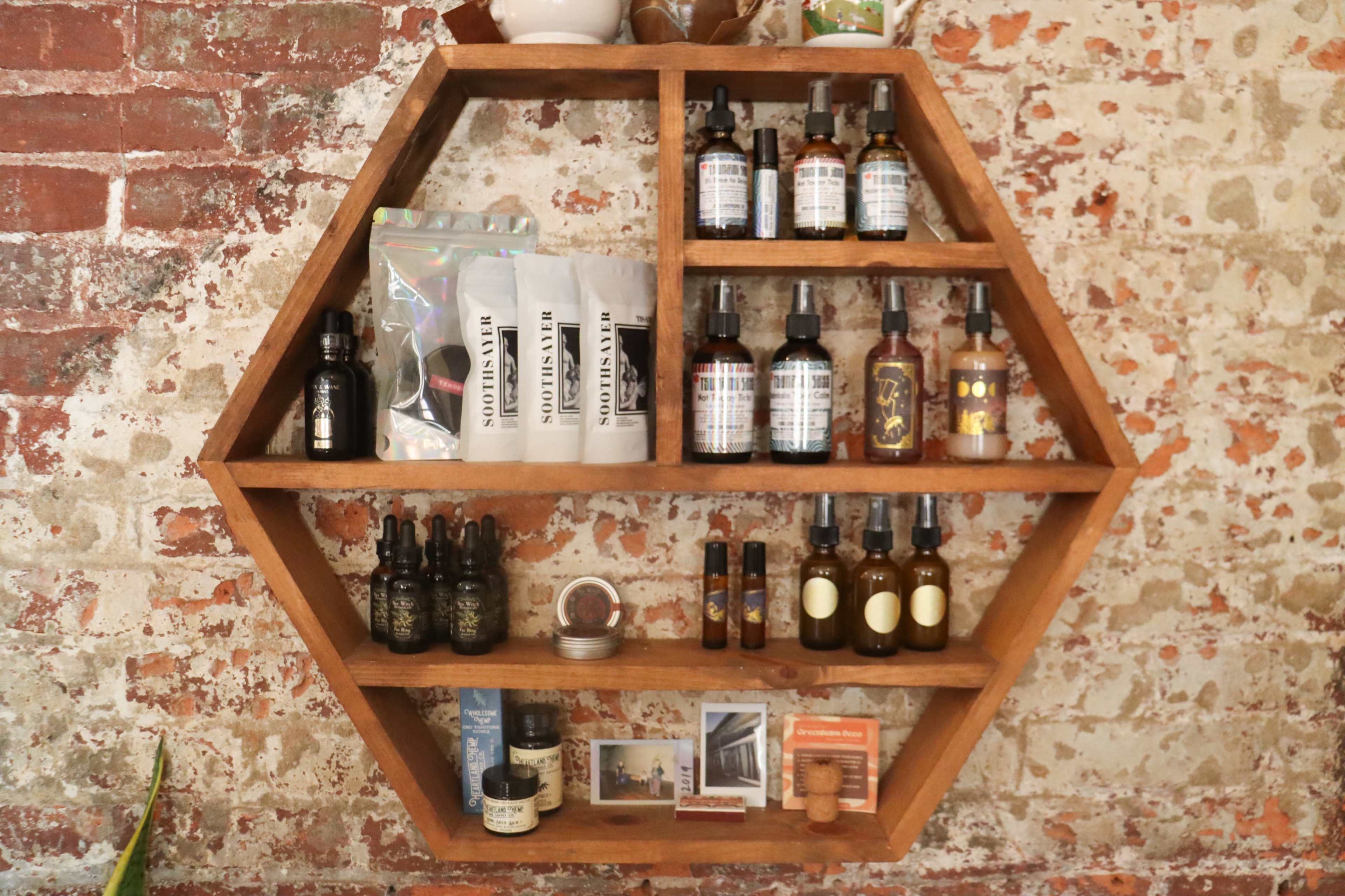 A honeycomb-shaped wooden shelf displays various bottles and packages of skincare products against a rustic brick wall.