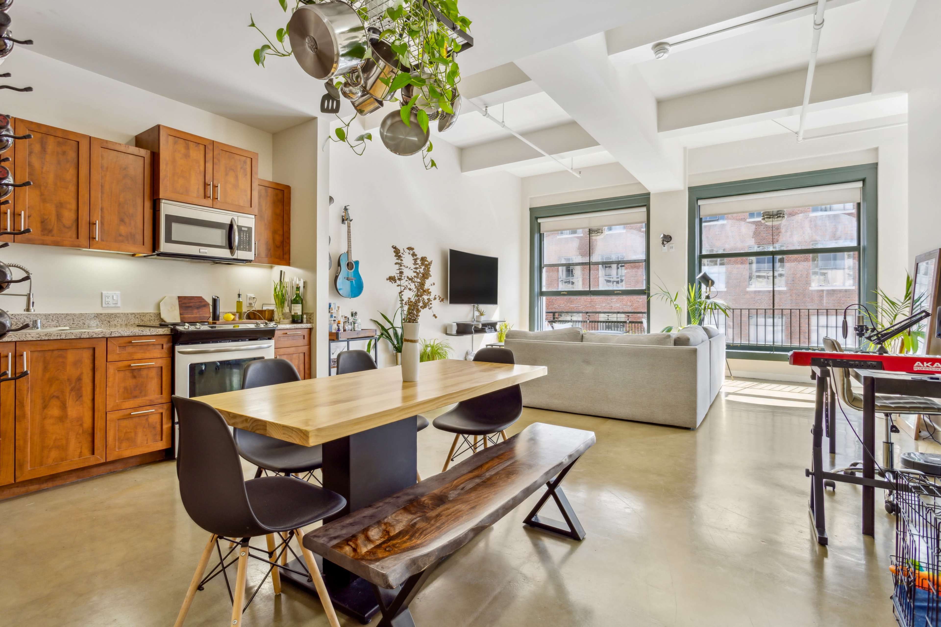 A modern open-concept kitchen and living area features wooden cabinets, a central dining table, and large windows with natural light.