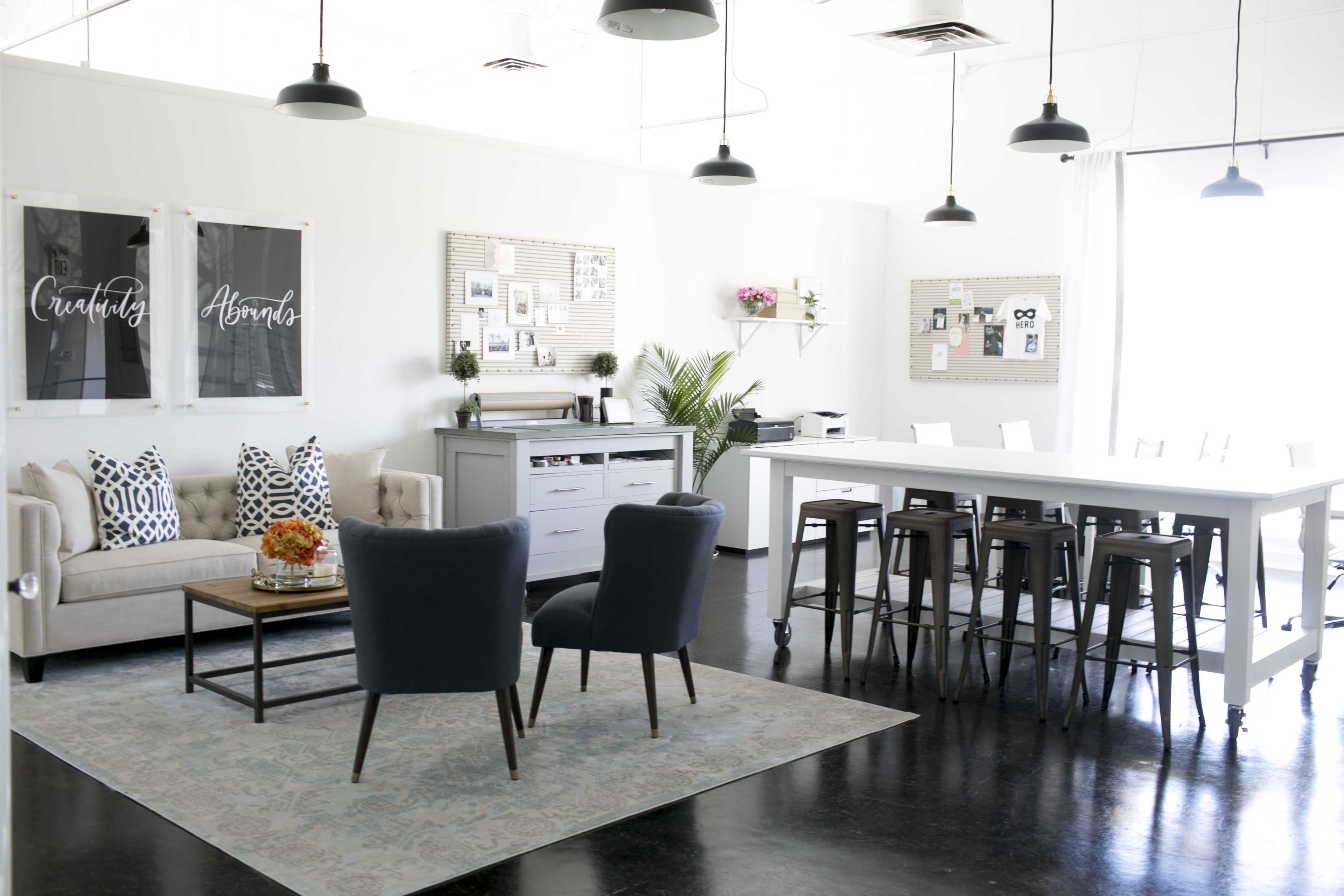 A modern interior features a living area with two chairs and a sofa, alongside a dining table with high chairs, all set against a bright, white backdrop.