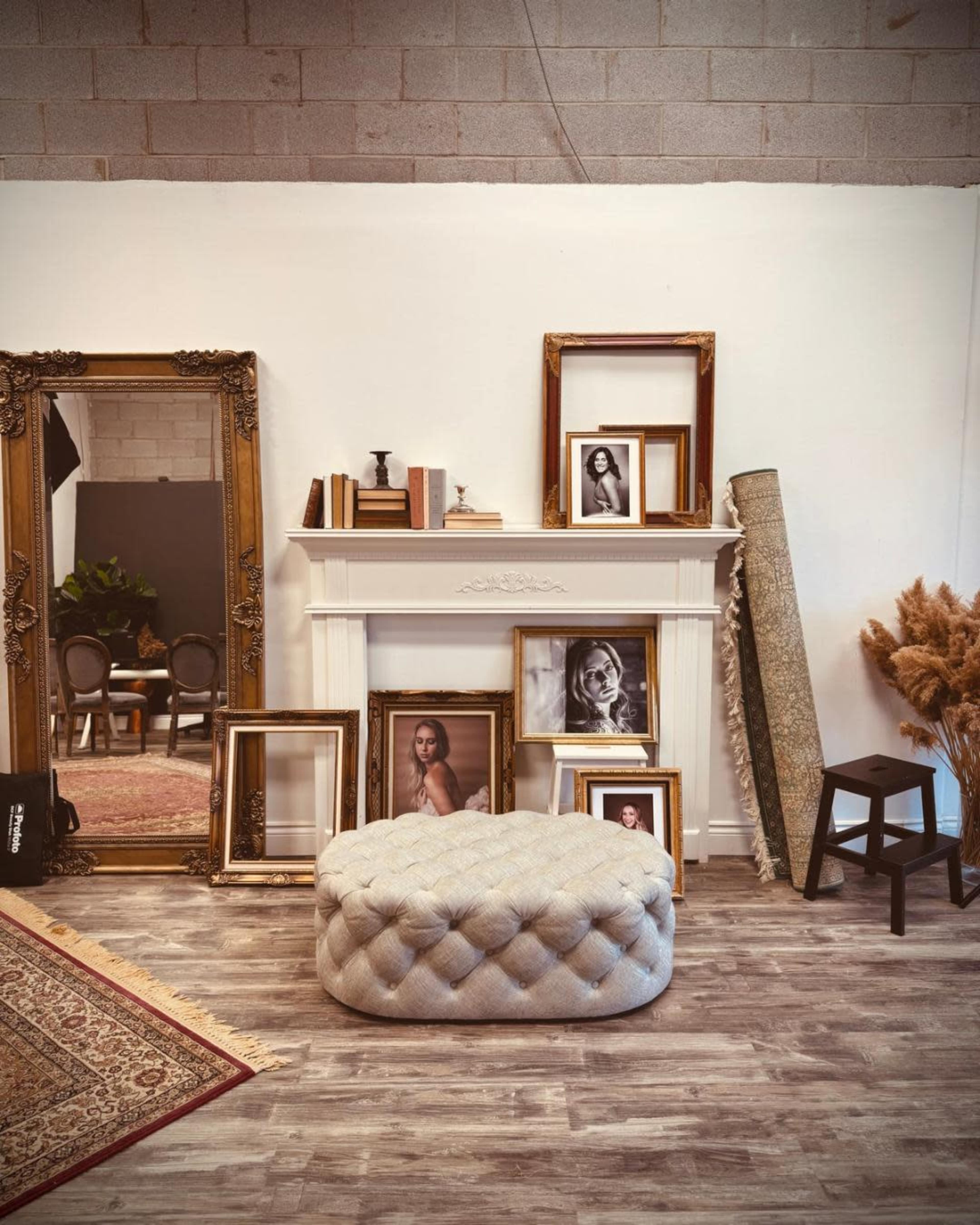 The scene features a decorative mantelpiece surrounded by framed photographs, a tufted ottoman, a rug, and a collection of various decorative items.