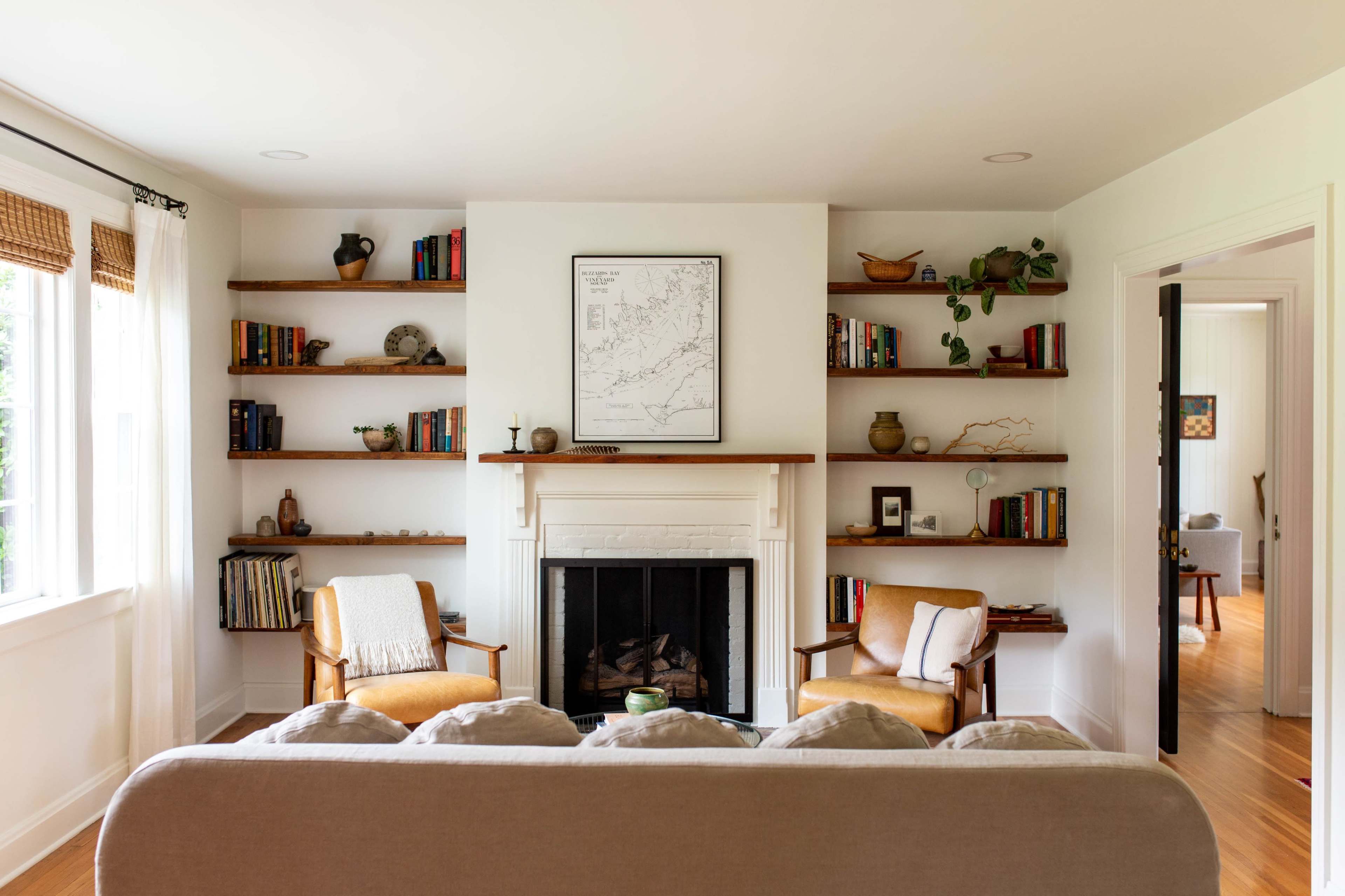 The image shows a living room with a fireplace flanked by bookshelves, a couch in the foreground, and two armchairs situated near the fireplace.