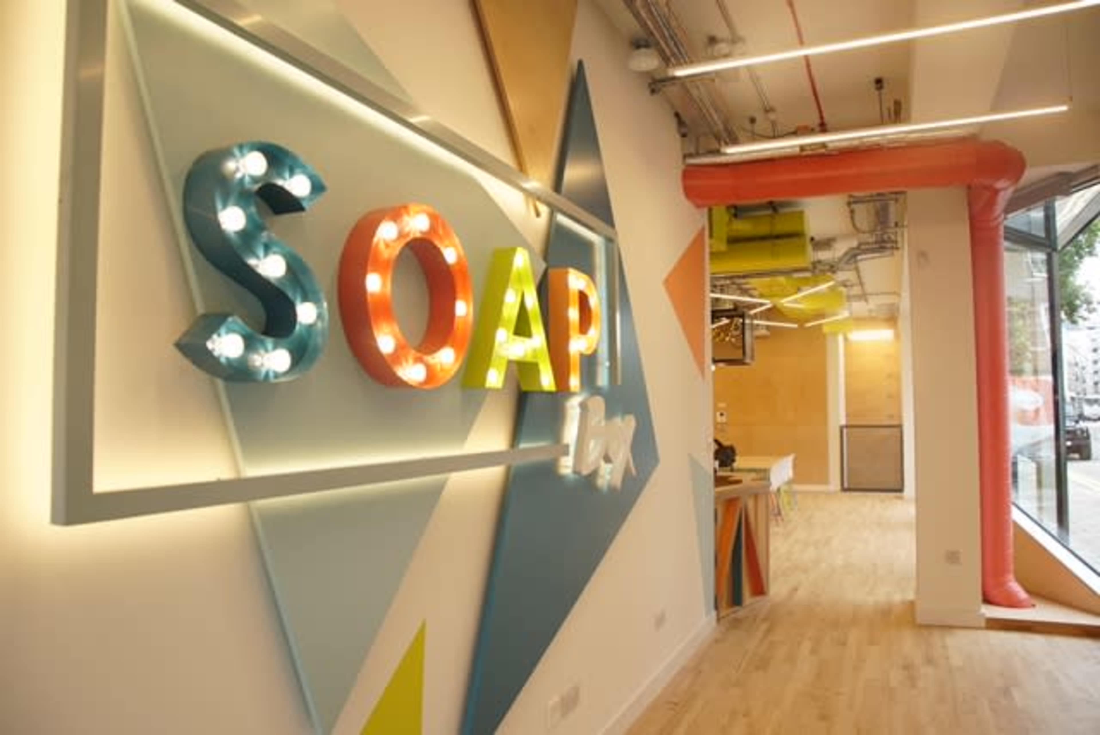 A brightly lit interior with colorful letters spelling "SOAP" on a wall, surrounded by geometric shapes and a modern workspace design.