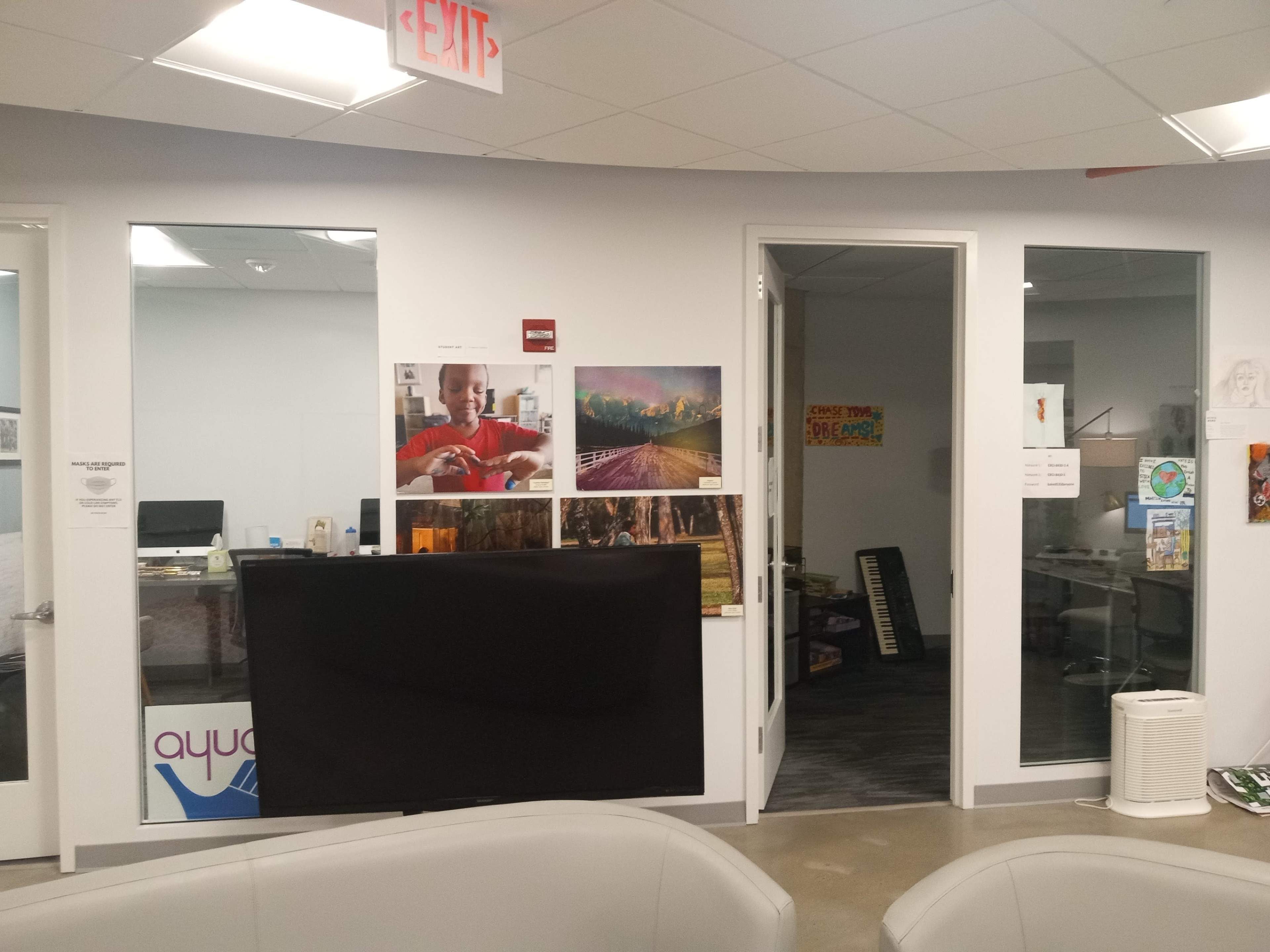 An office space with glass doors, featuring framed photographs on the walls and a black panel obscuring part of the view.