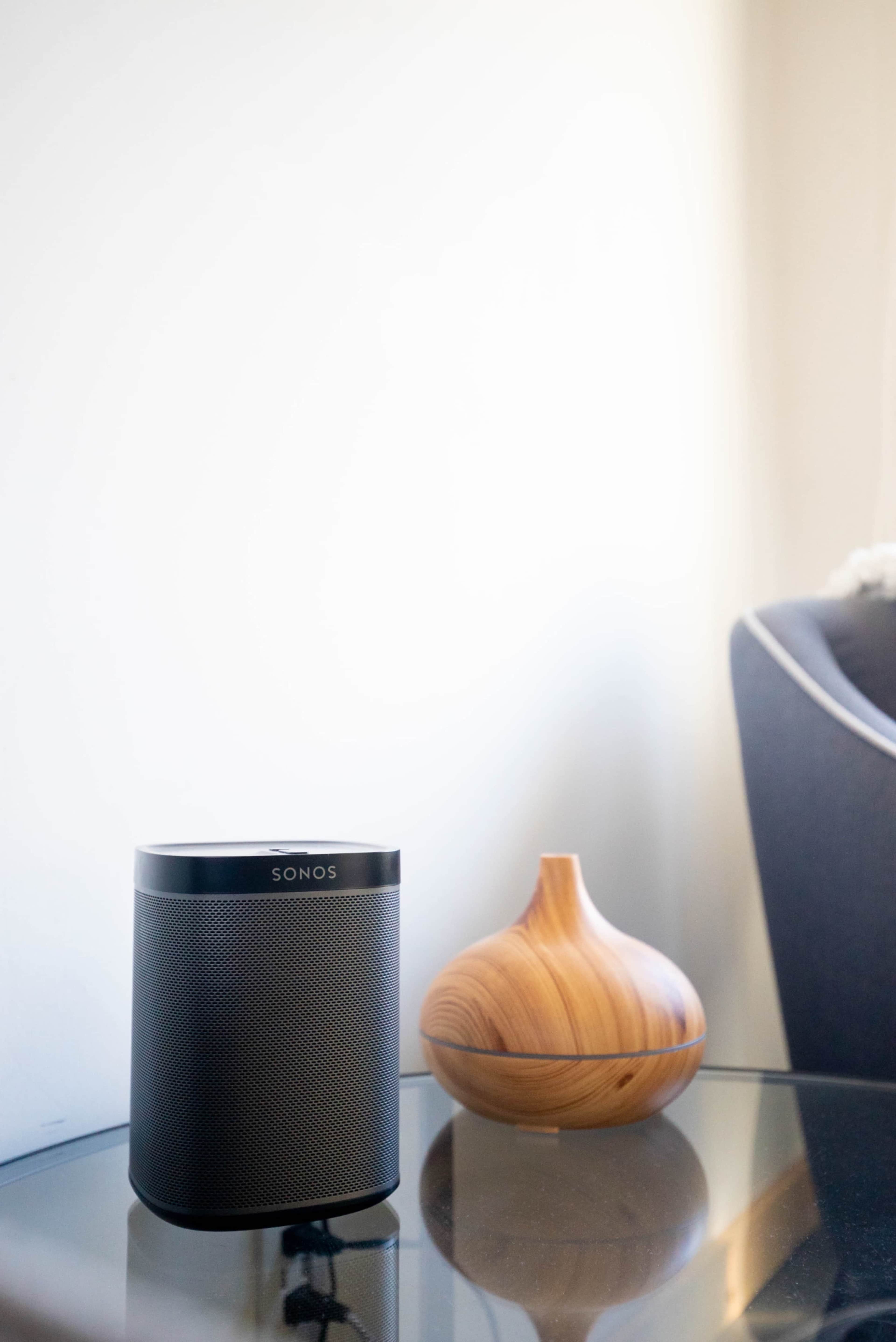 A black Sonos speaker sits on a glass table next to a wooden vase.