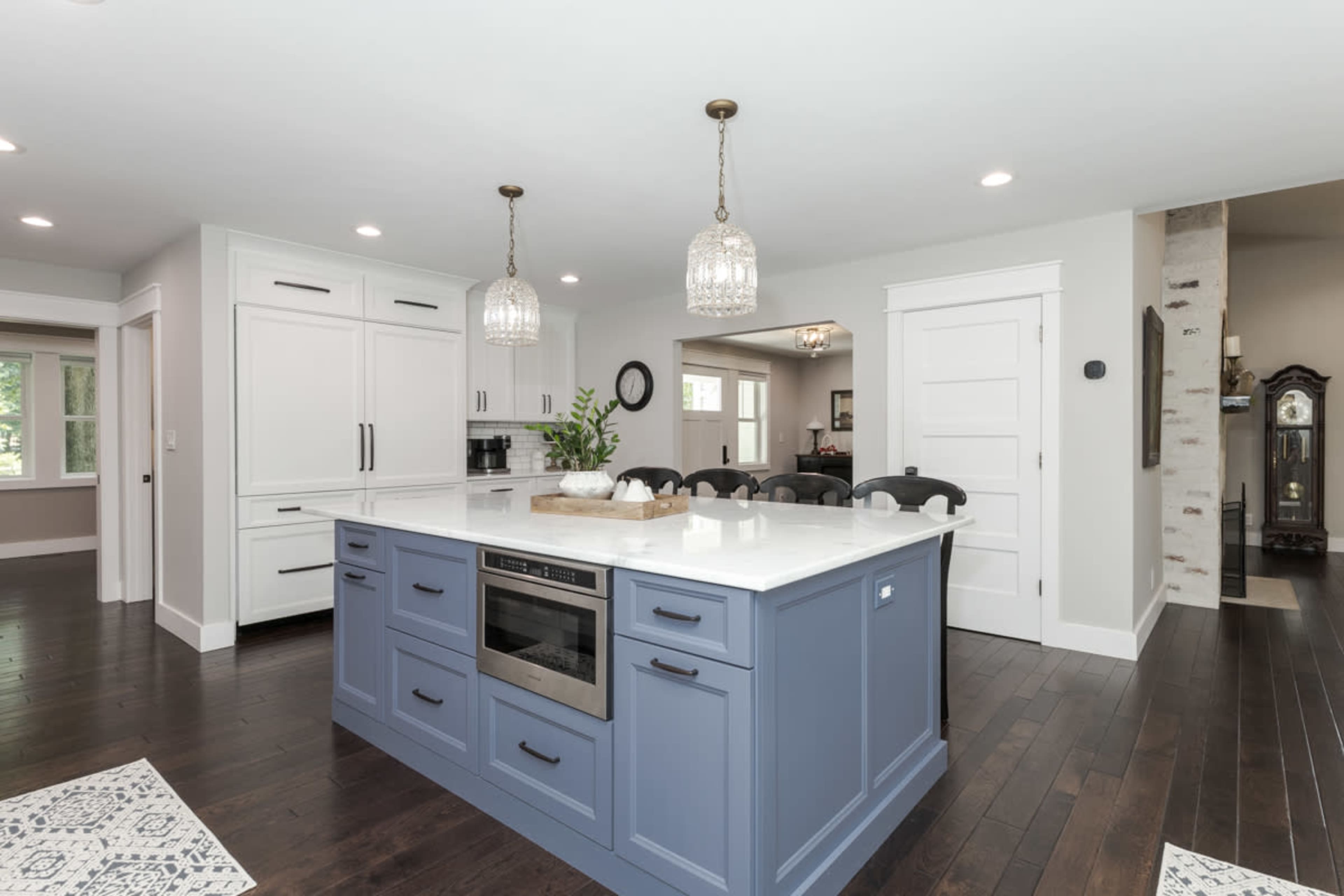A modern kitchen features a blue island with a white countertop, pendant lights, and dark hardwood flooring.
