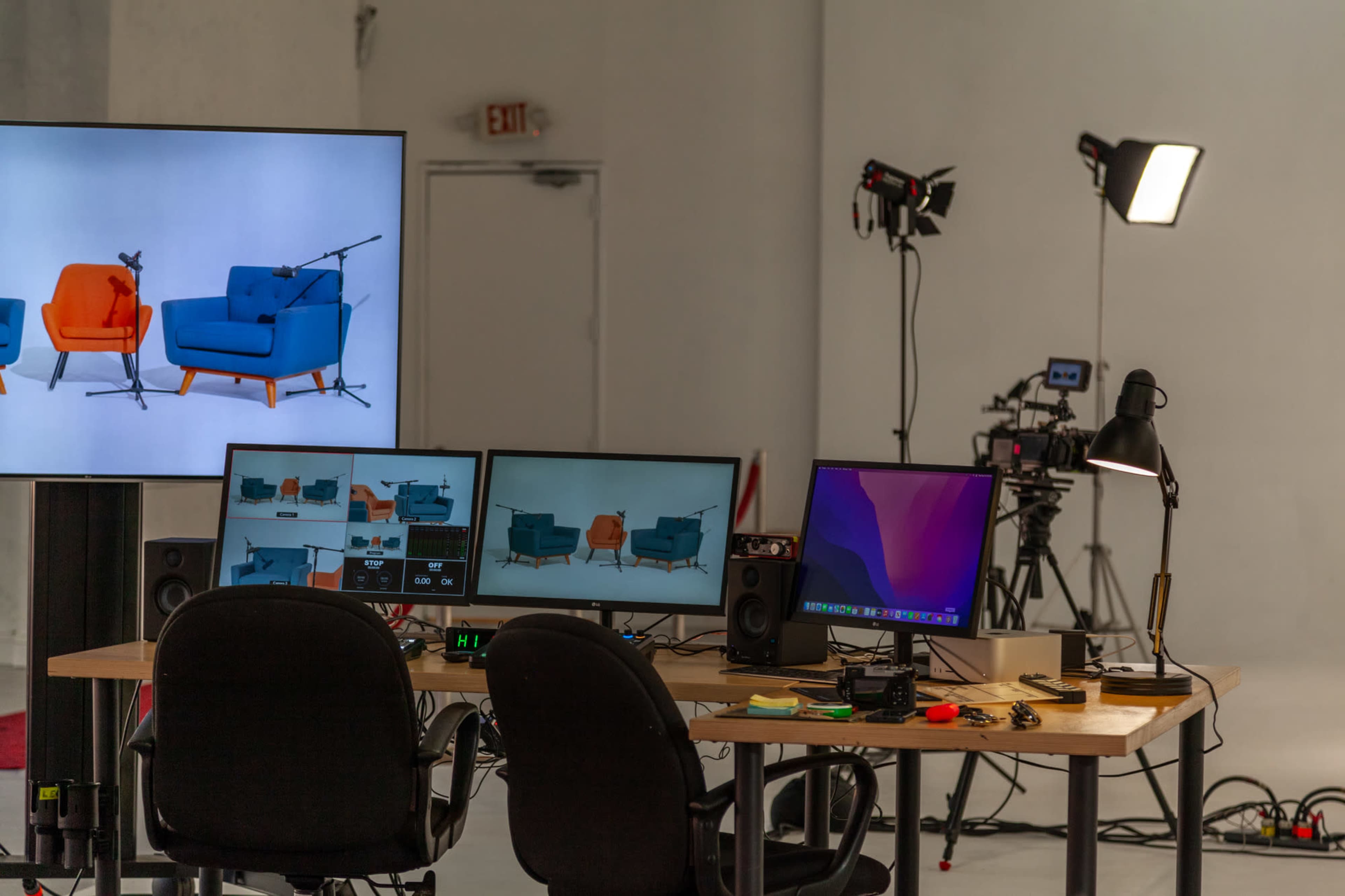 A modern workspace is set up with multiple computer monitors displaying images of chairs, alongside cameras and lighting equipment in a well-lit studio.