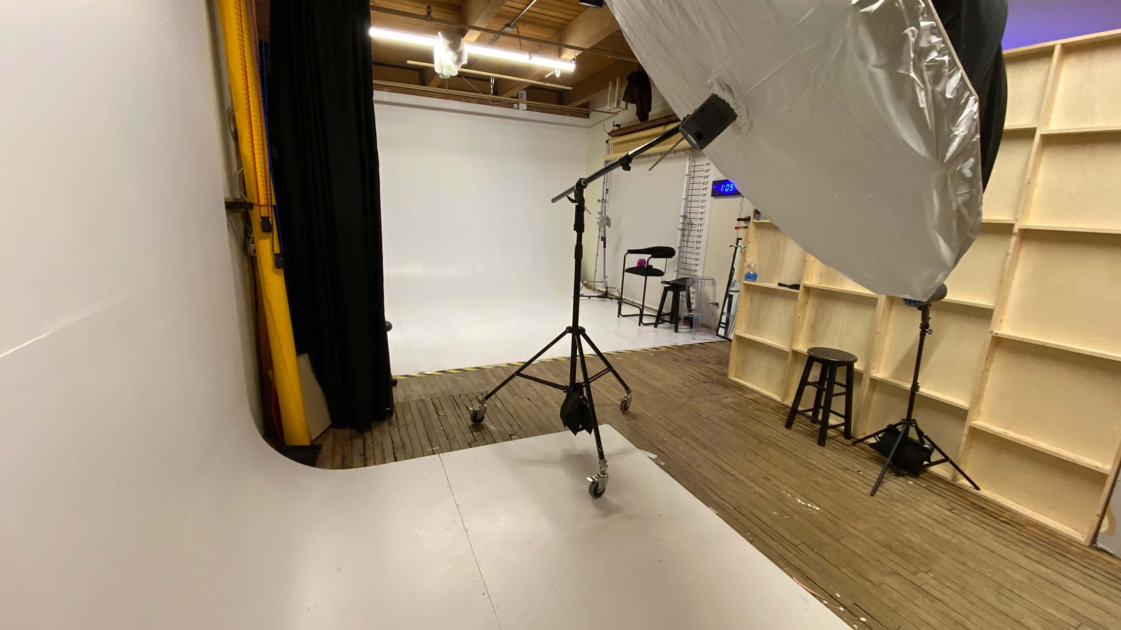A photography studio with a seamless white backdrop, a lighting setup on a stand, and wooden flooring.