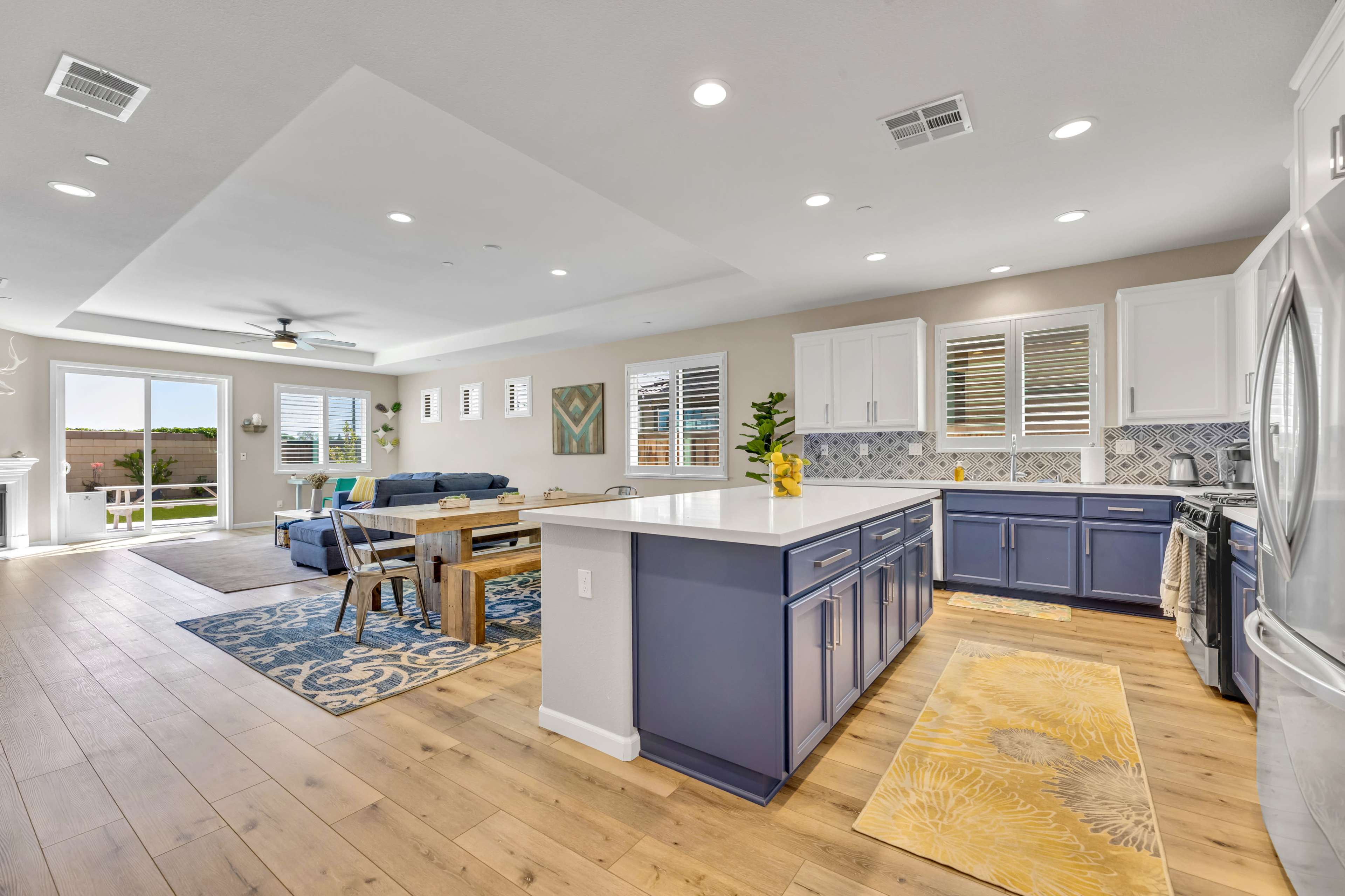 A modern kitchen and living area with blue cabinetry, a white island, and large windows that open to a patio.