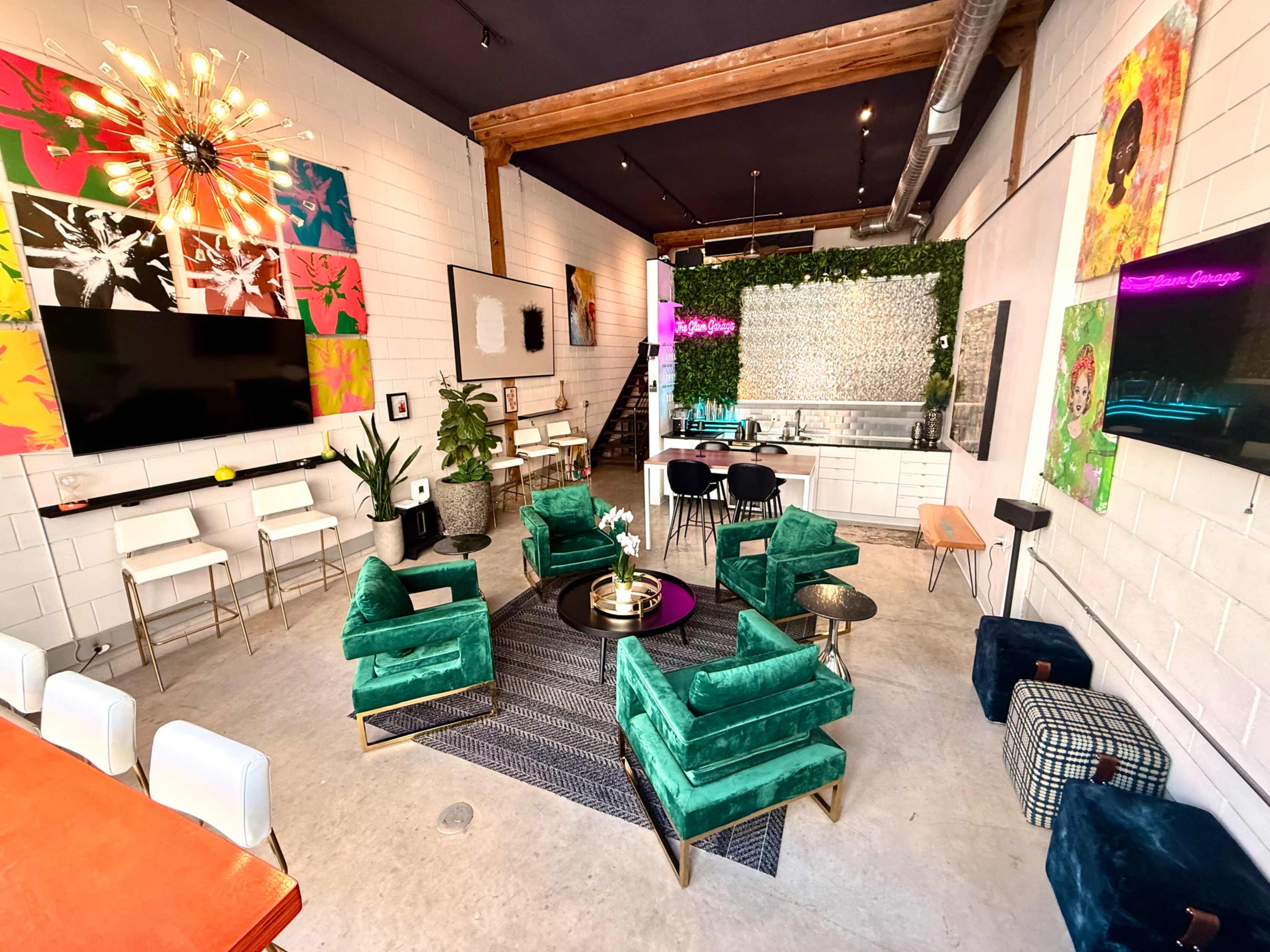 The image shows a modern, open-concept lounge area with green upholstered chairs, a large communal table, and a mix of colorful artwork on the walls.