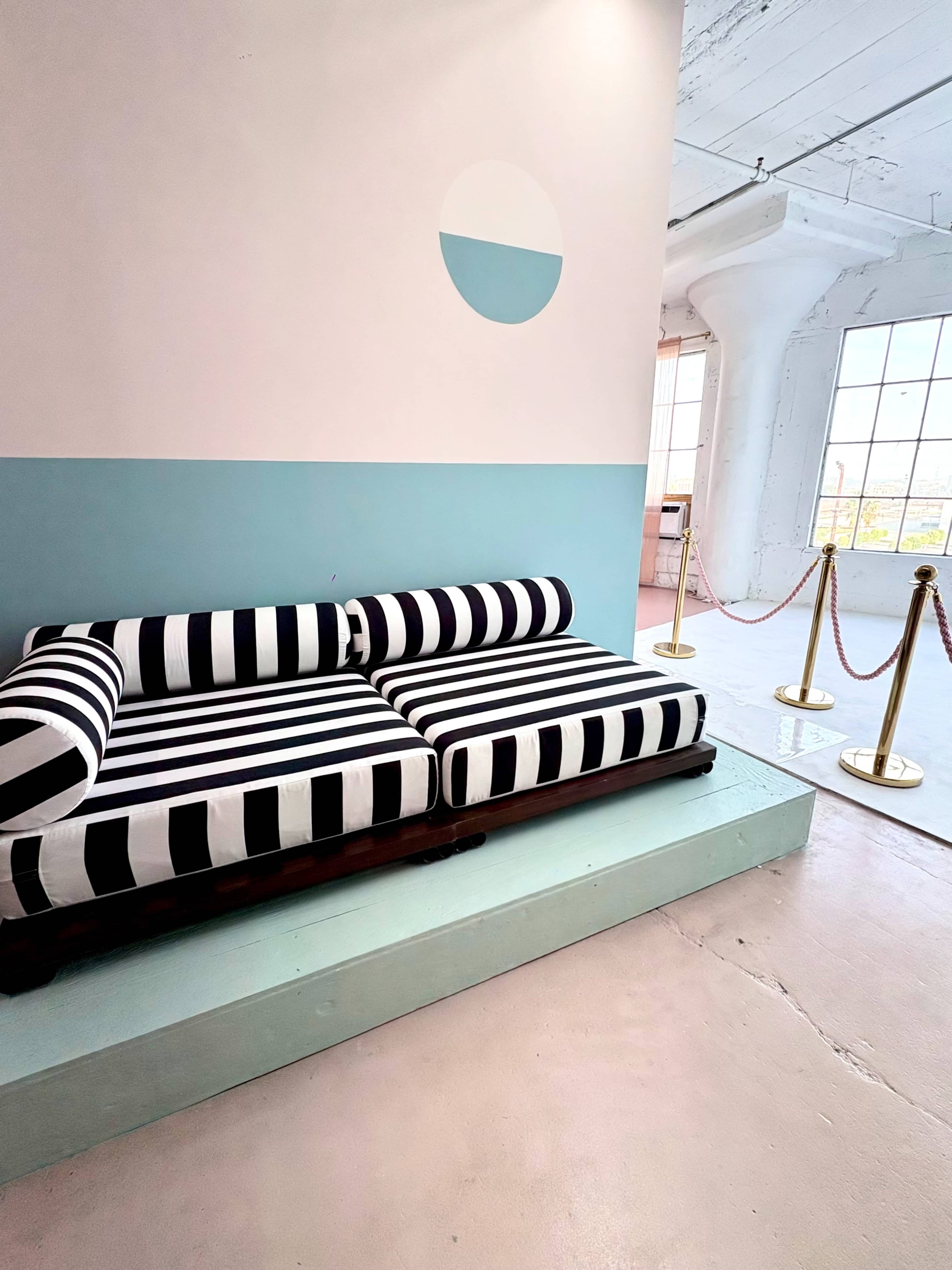 The image features a modern interior space with a black and white striped sofa on a raised platform, complemented by a light blue-painted wall and a minimalistic circular artwork above.
