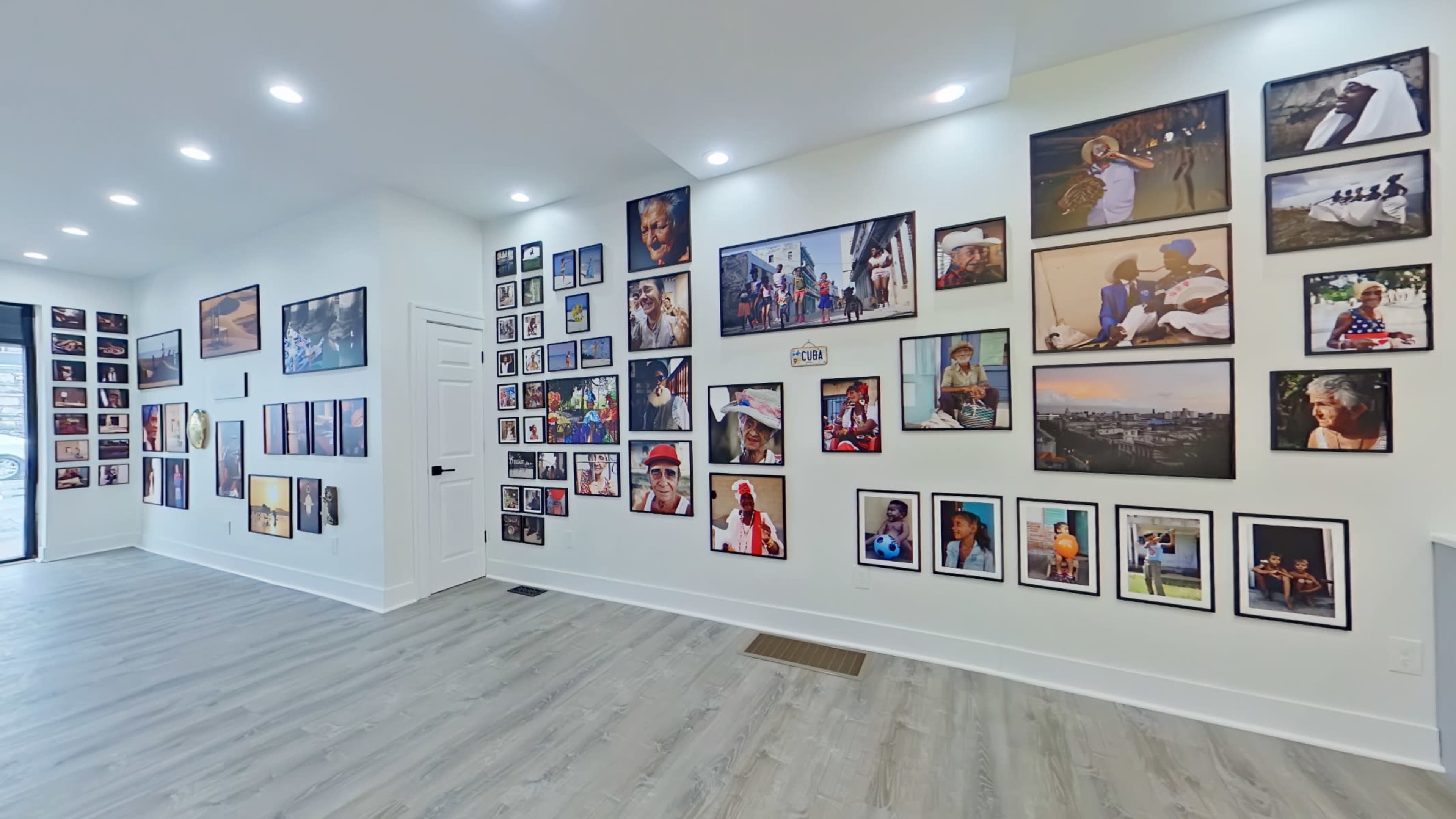 The image shows a spacious room with white walls adorned with an array of framed photographs in various sizes, creating a gallery-like atmosphere.