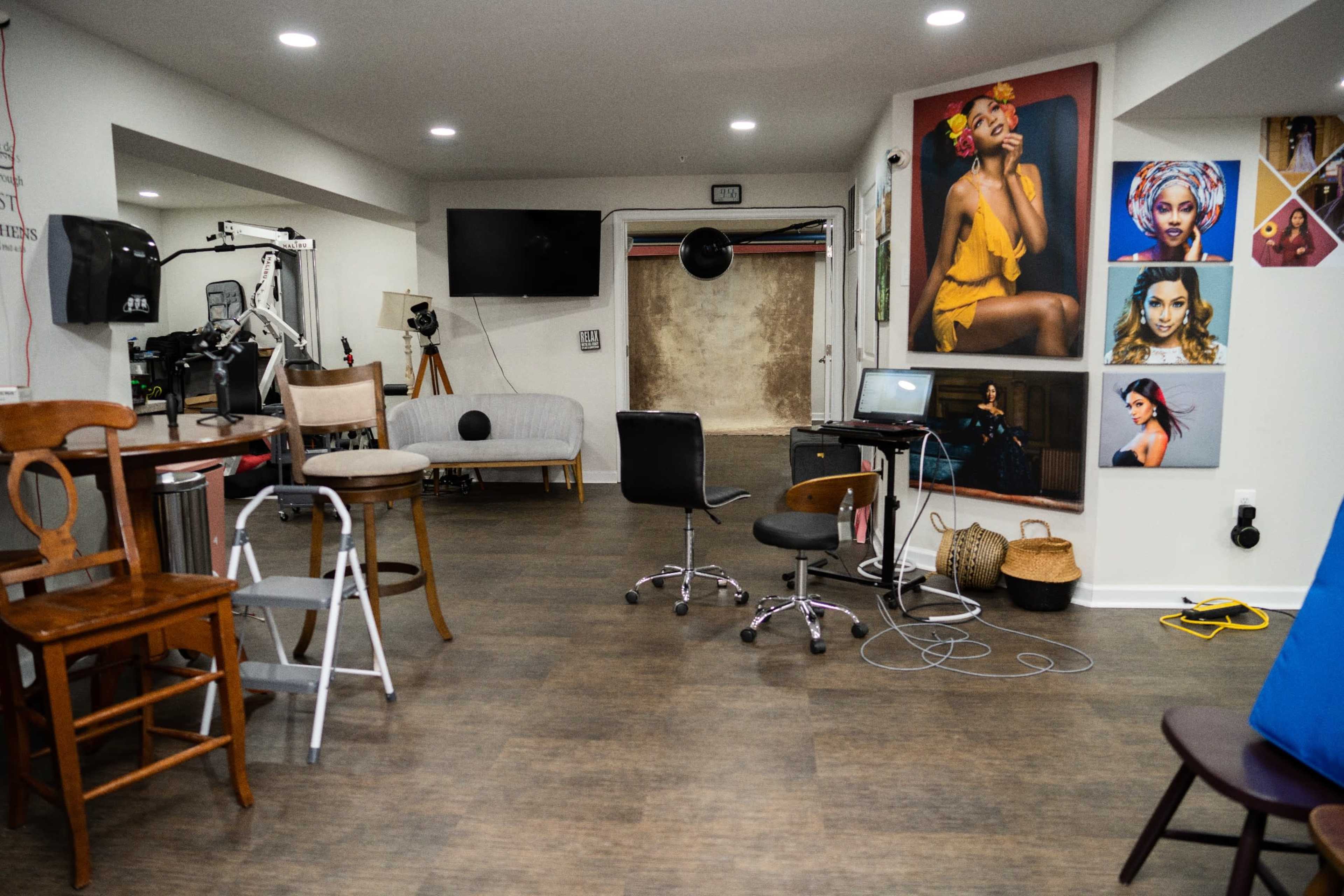 The image shows a spacious studio with various chairs, a couch, and multiple framed portraits hanging on the walls.