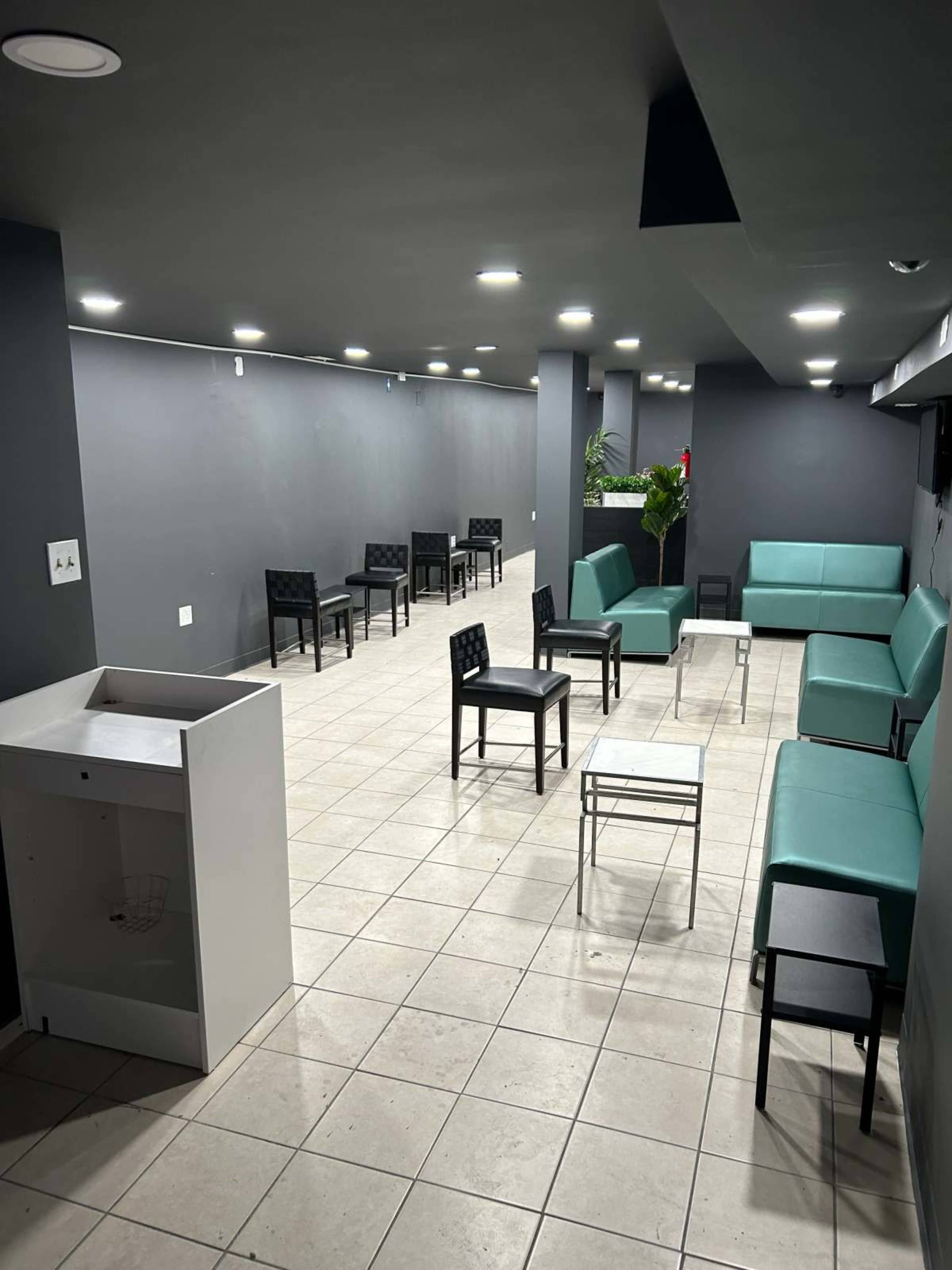 A spacious indoor area with several black and teal seating arrangements and a small table in the center, set against grey walls and tiled flooring.