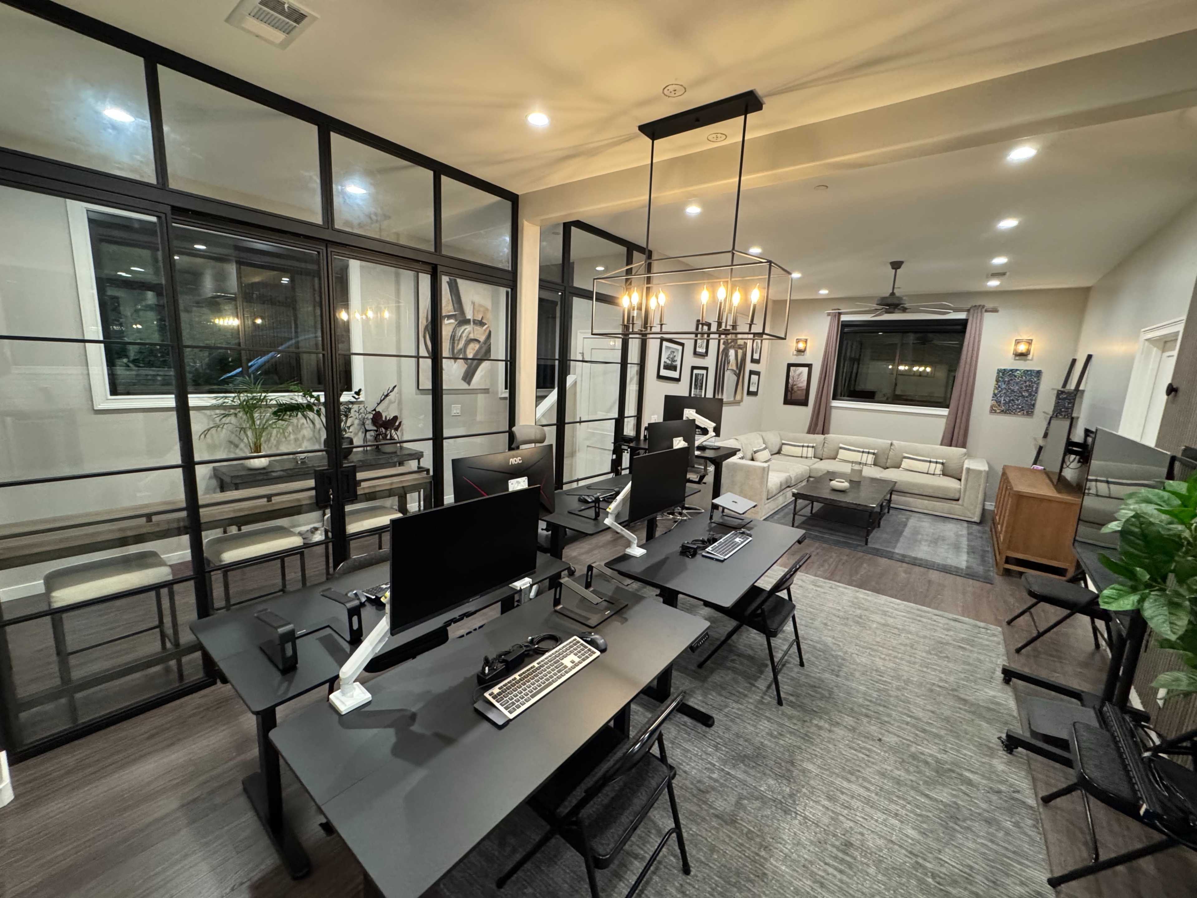 The image shows a modern office space featuring multiple workstations with computers, surrounded by glass walls and a lounge area with a sofa and seating.