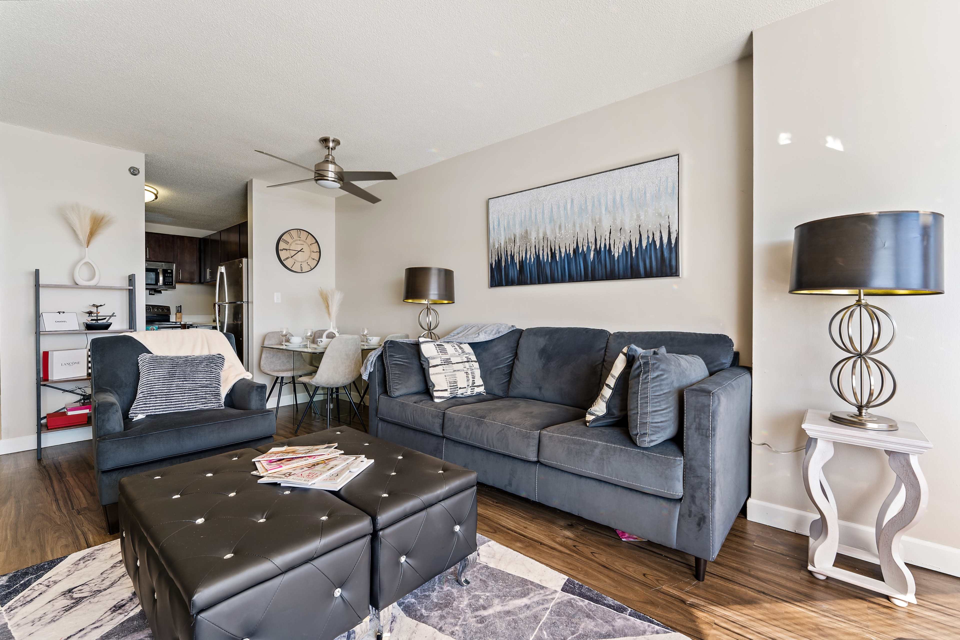 The living area features a dark sofa, two lamps, a coffee table with magazines, and a dining space with a round table in the background.