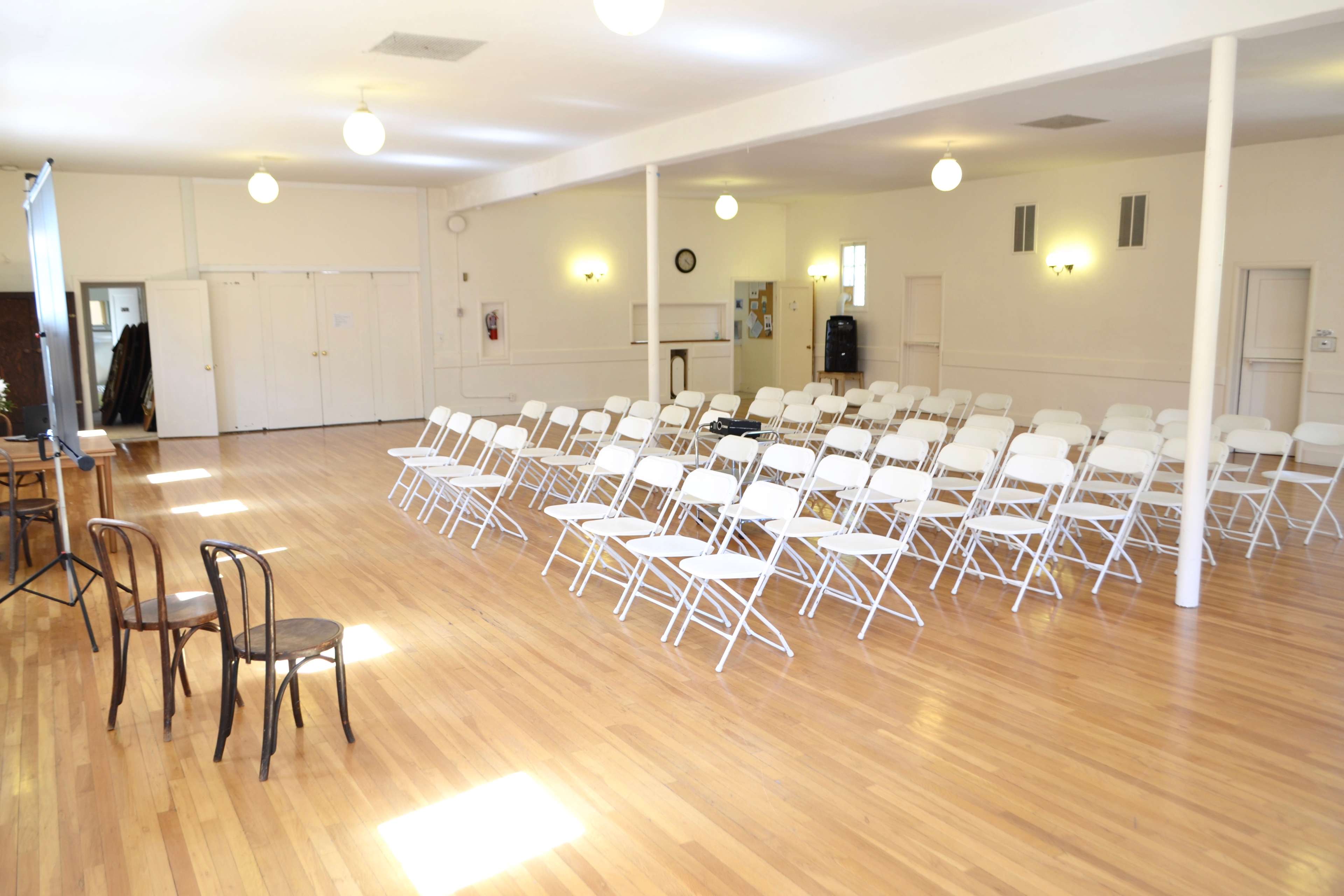 A brightly lit hall features rows of white folding chairs arranged facing a small stage.