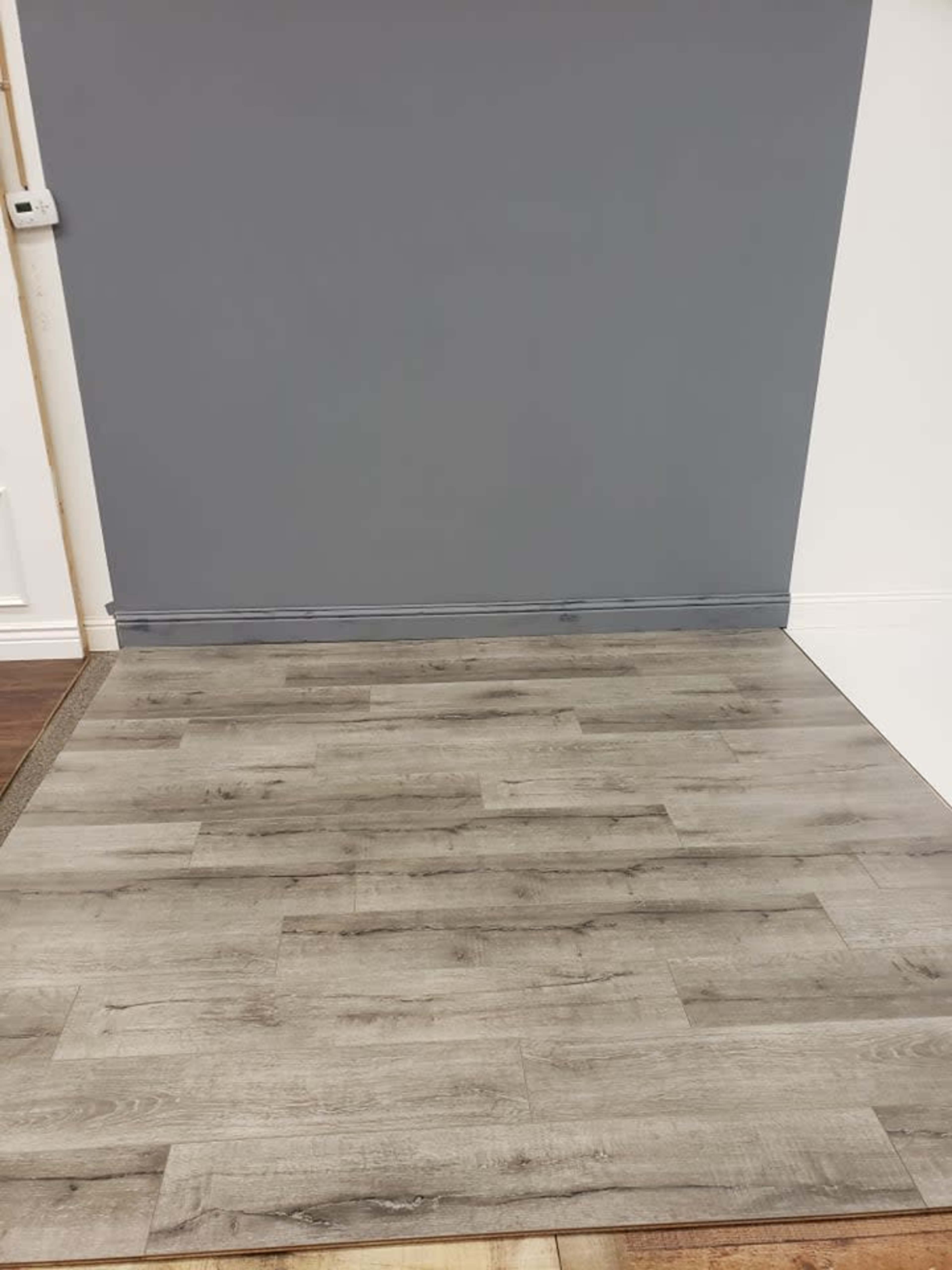 A section of a room with light gray laminate flooring and a dark gray wall.