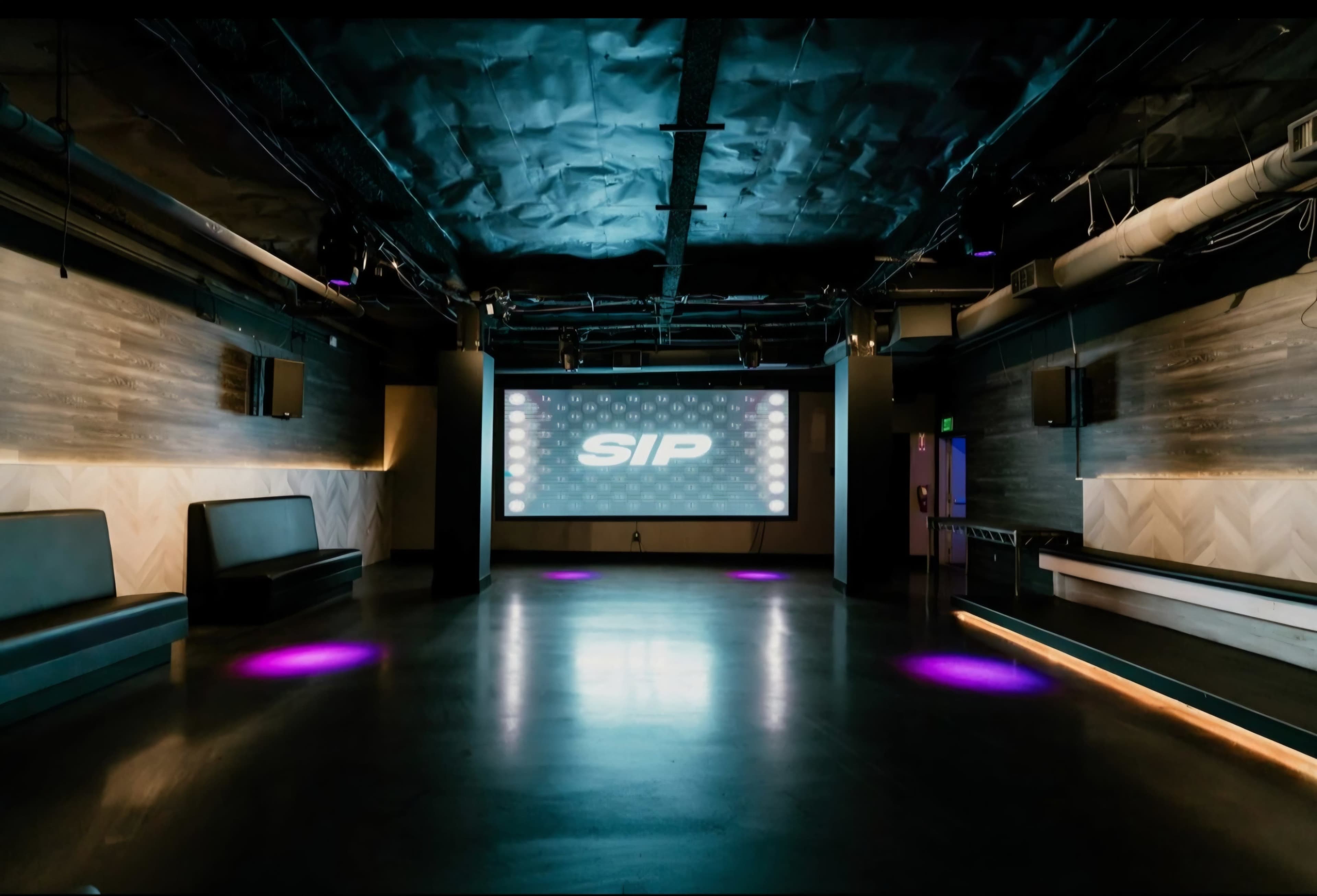 The image shows a spacious, modern event venue with a large screen displaying the word "SIP" and purple lighting on the floor.