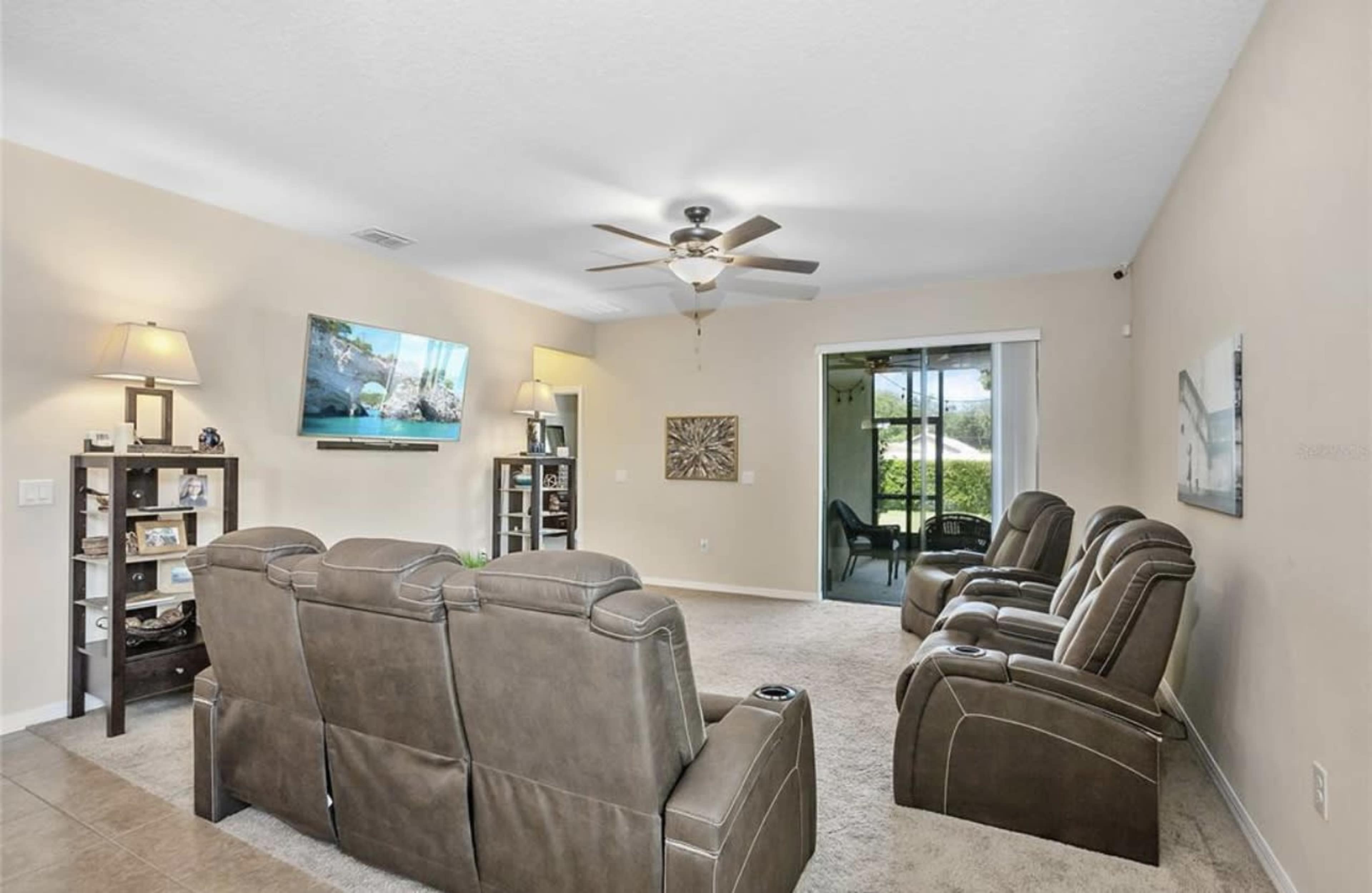 The living room features a set of brown reclining chairs, a wall-mounted television, and a sliding glass door leading to an outdoor space.