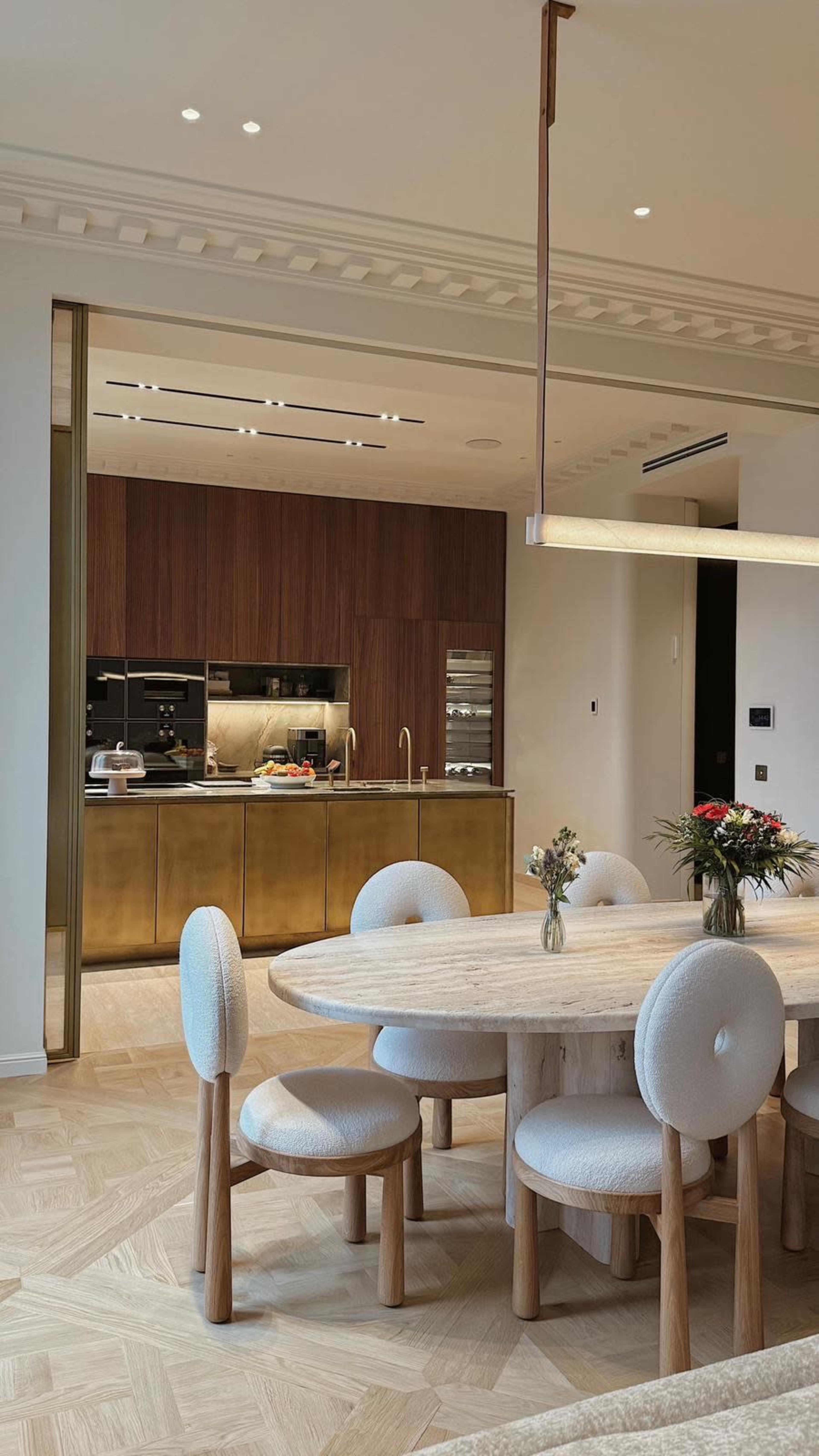 A modern kitchen and dining area features a wooden table surrounded by round, upholstered chairs, with a sleek kitchen in the background.
