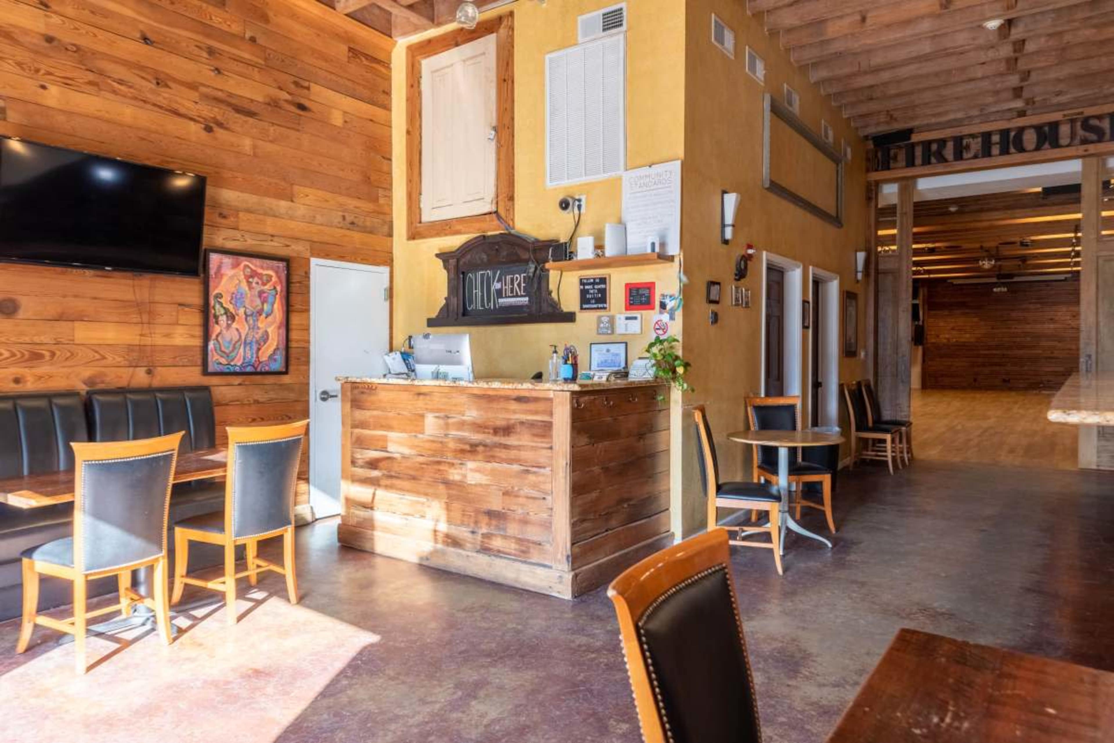 The image shows the interior of a restaurant featuring wooden walls, a reception counter, and seating arrangements with tables and chairs.