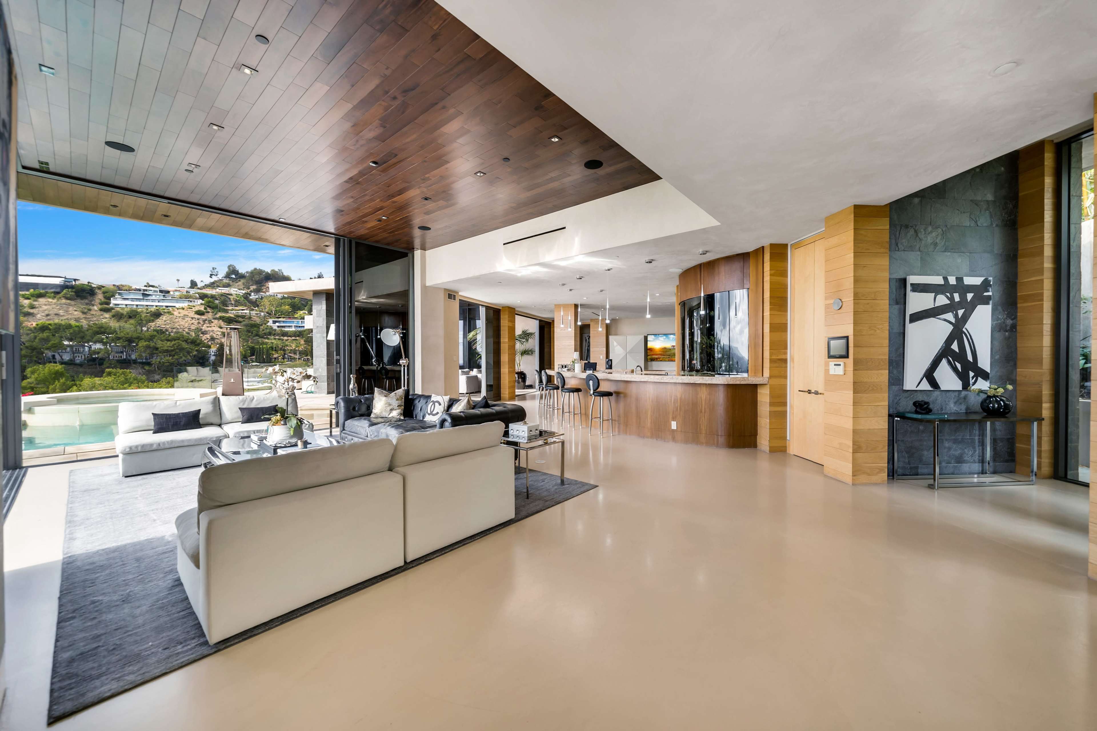 The image shows a modern open-concept living space with a view of the outdoors, featuring a sleek kitchen and a comfortable seating area.