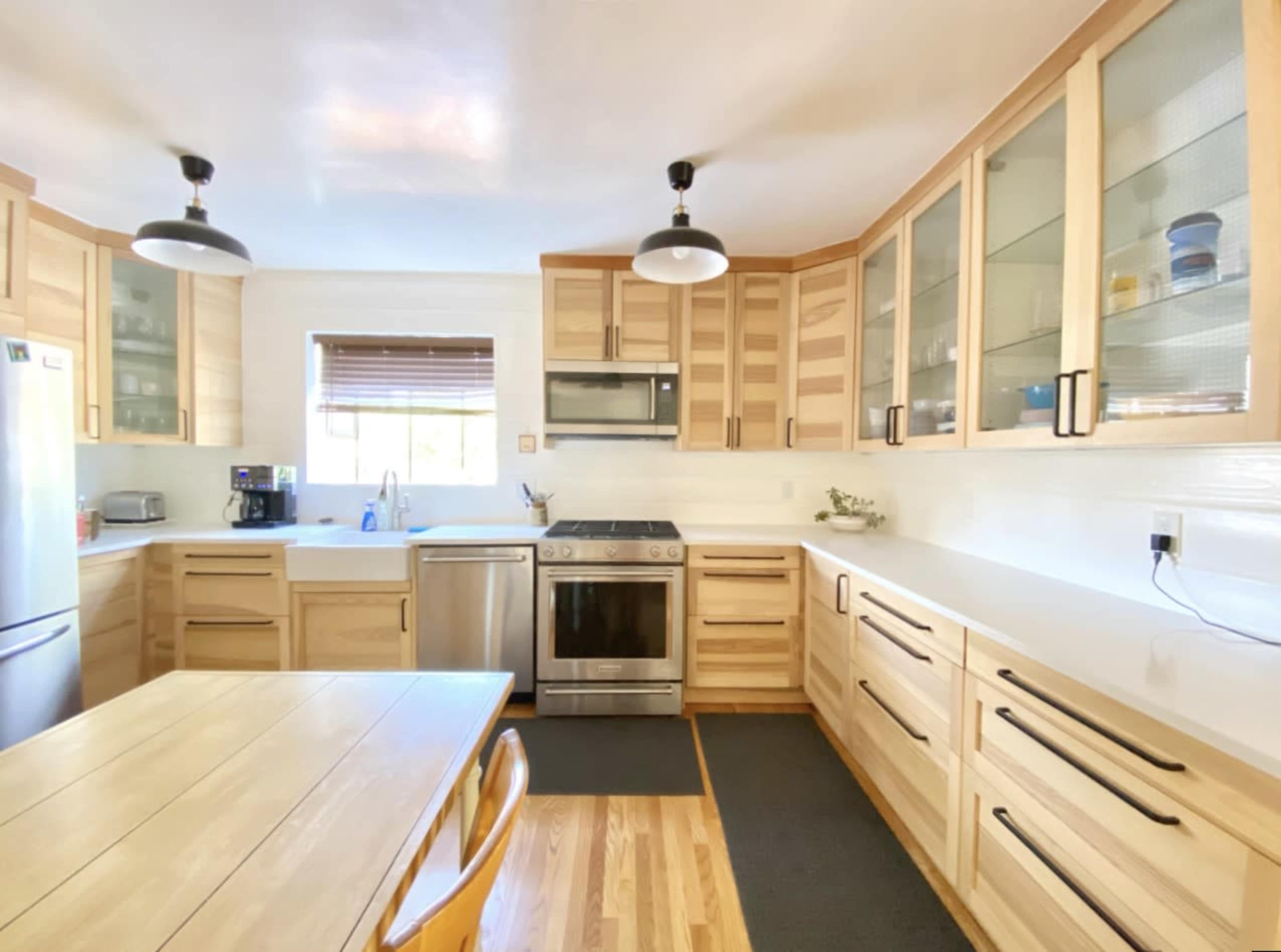 The kitchen features wooden cabinetry, stainless steel appliances, and a dining table in a well-lit space.