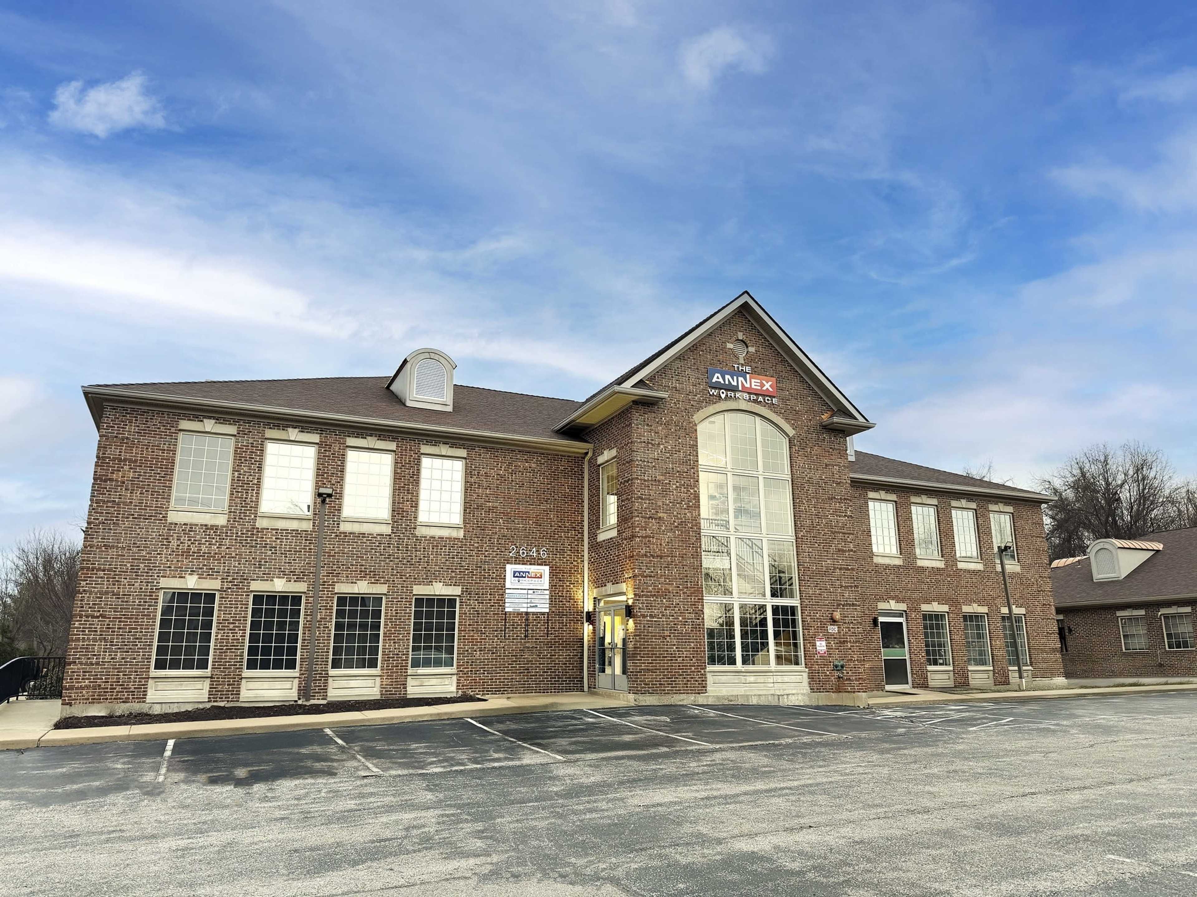 The image shows a brick office building with a large arched entrance and multiple windows under a clear blue sky.